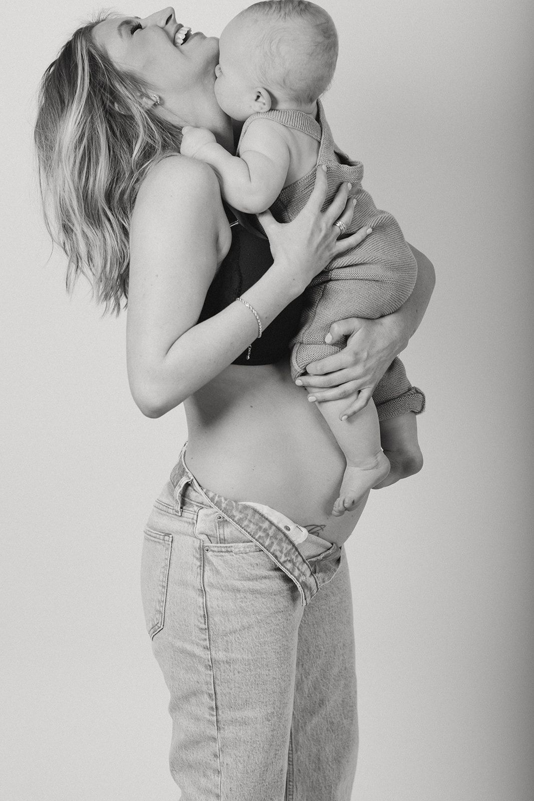 Black and white intimate portrait series of a mother holding and kissing her baby in natural lighting.