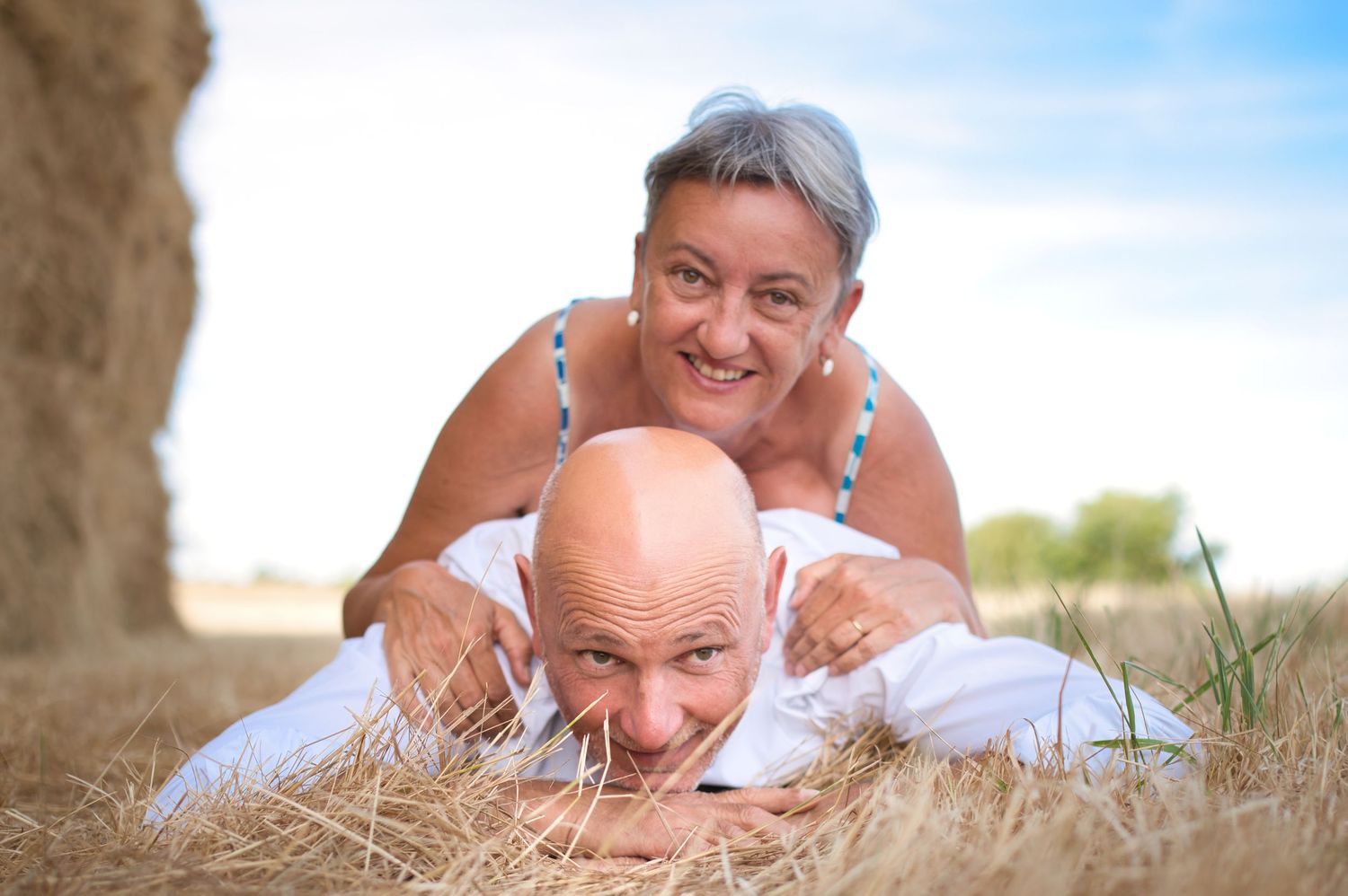 Couple relaxing on hay field during a sunny afternoon photoshoot.