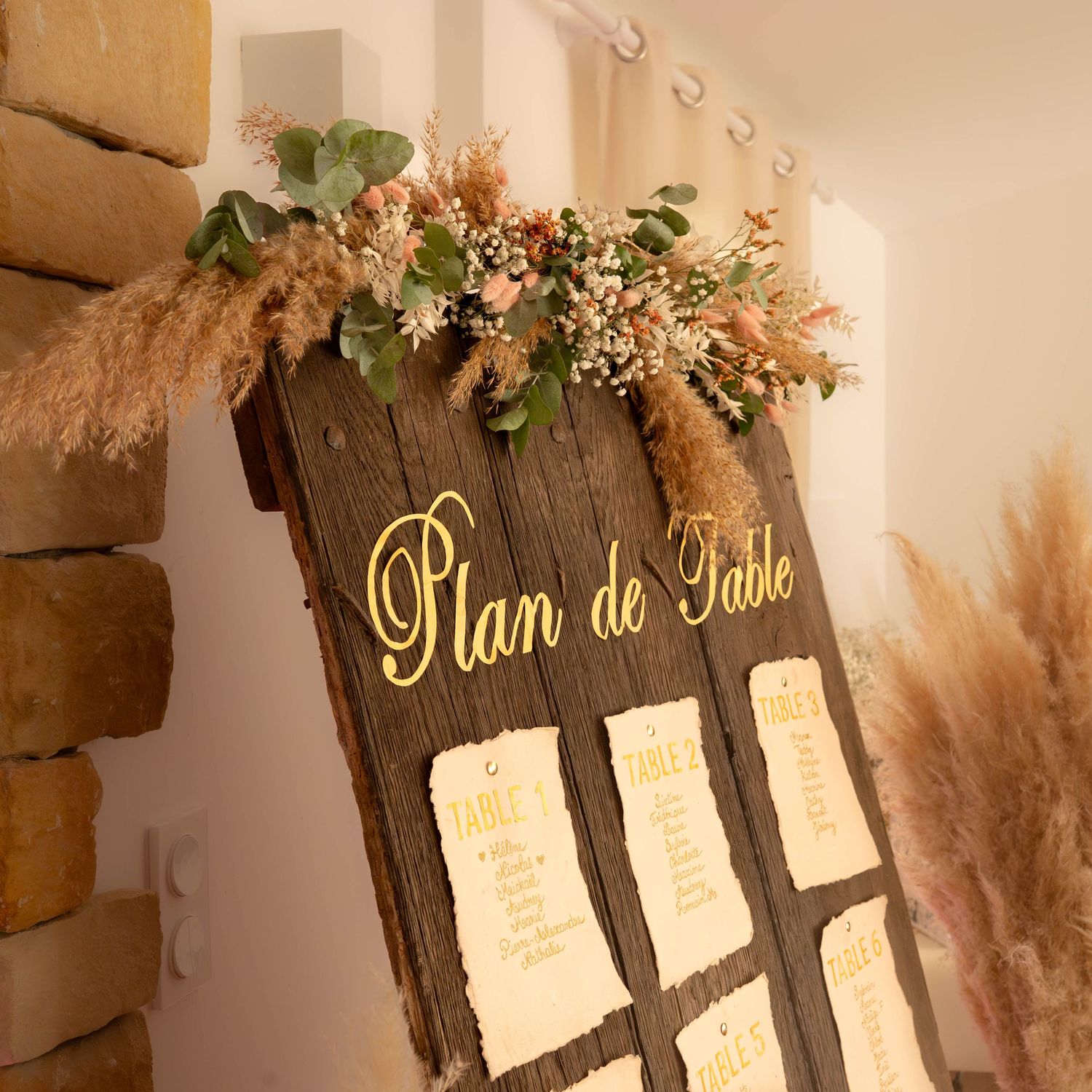 Rustic wooden seating chart display with pampas grass and floral decorations for a wedding reception.