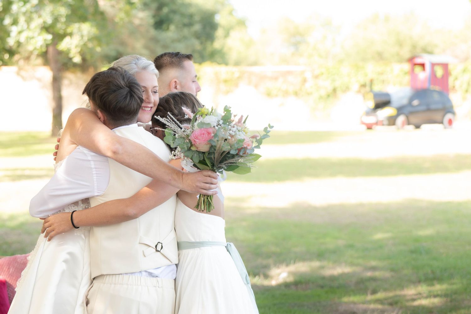 A couple embraces during their outdoor wedding ceremony in a sun-dappled garden setting.
