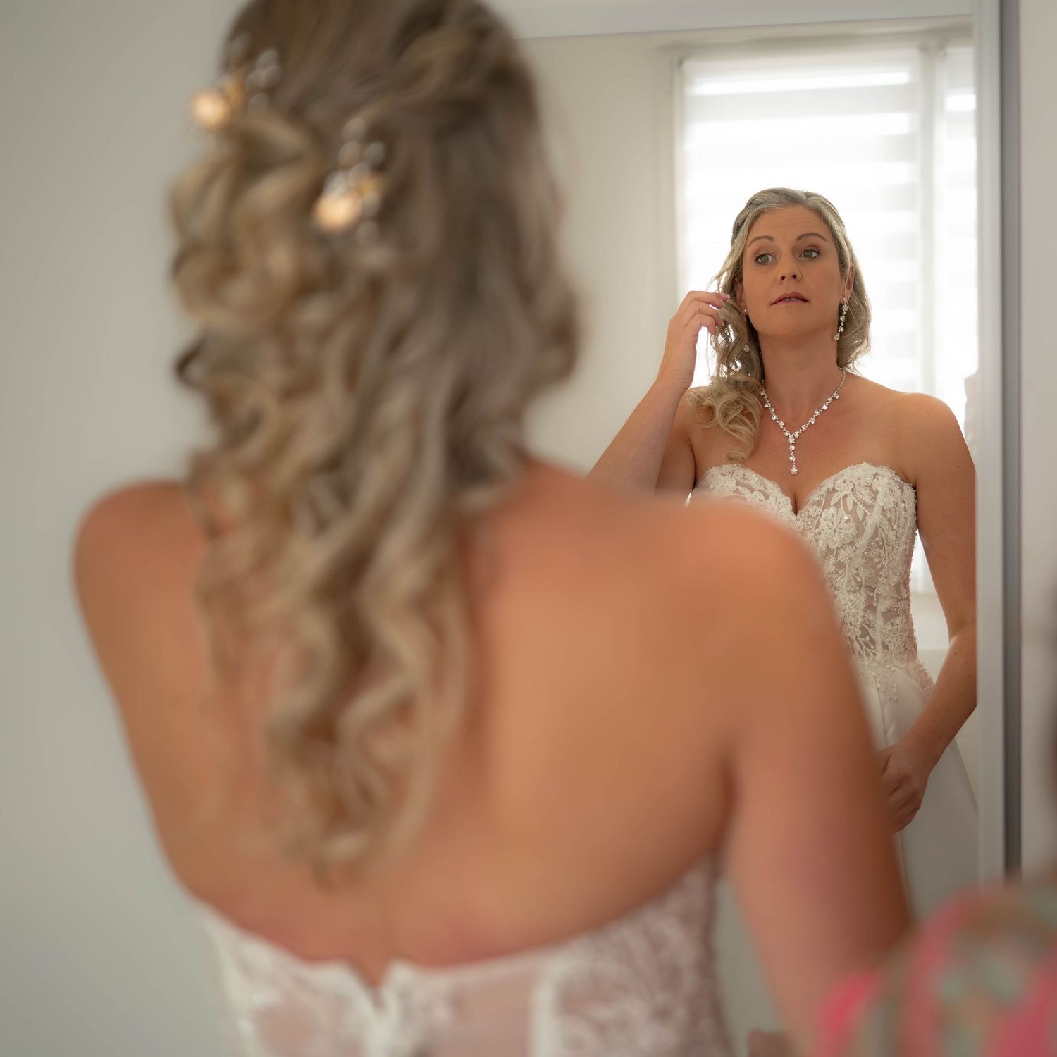 Multiple shots of a bride getting ready in a white wedding dress near a bright window.