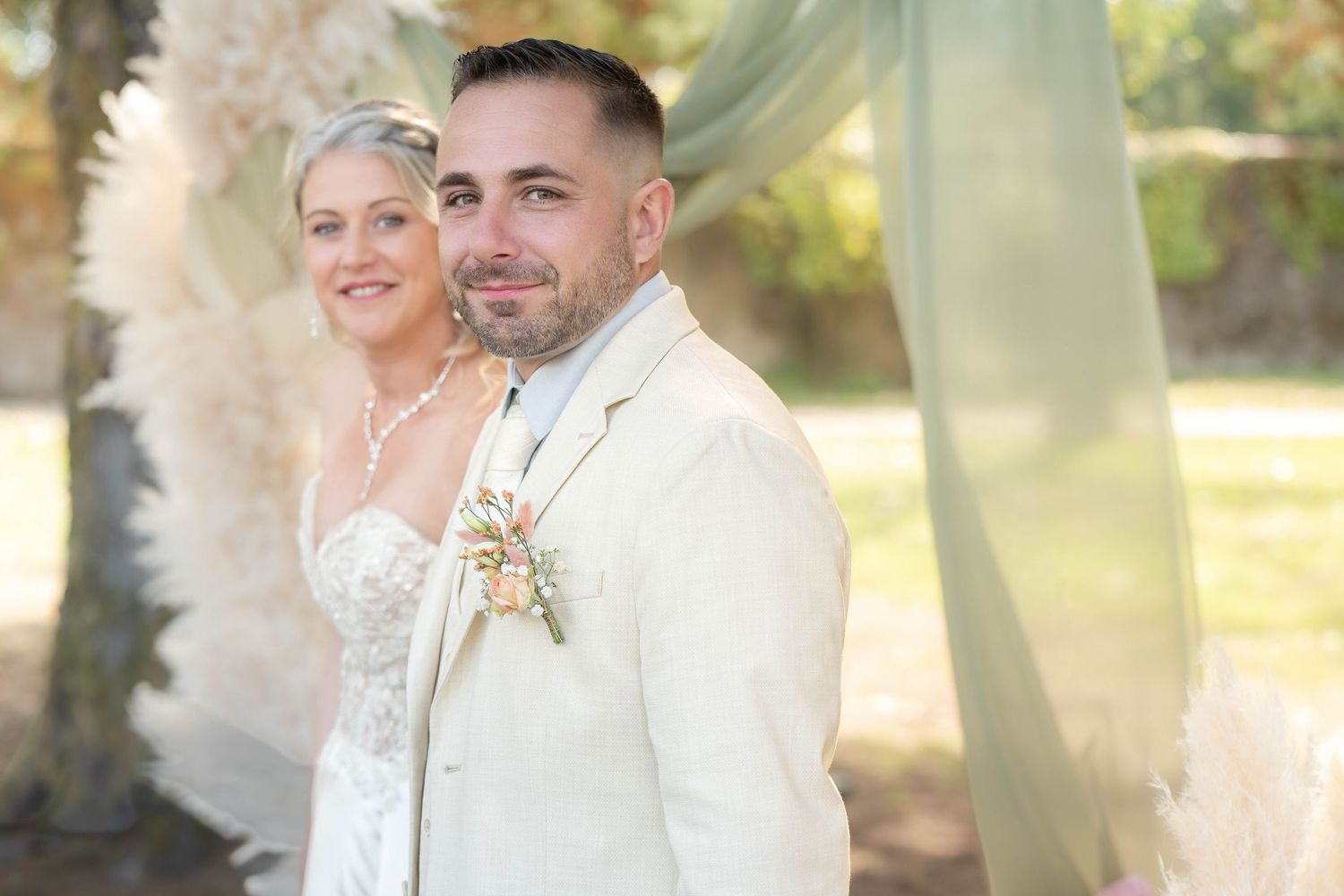 A couple embraces during an outdoor wedding photoshoot in a sunlit garden setting.