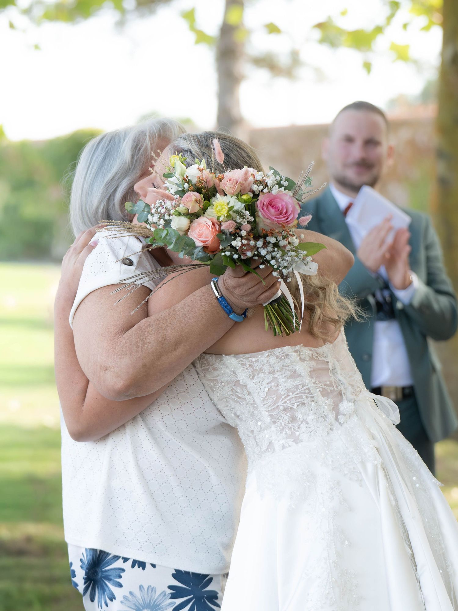 Close-up of bridal bouquet with pink and peach flowers against white lace dress.