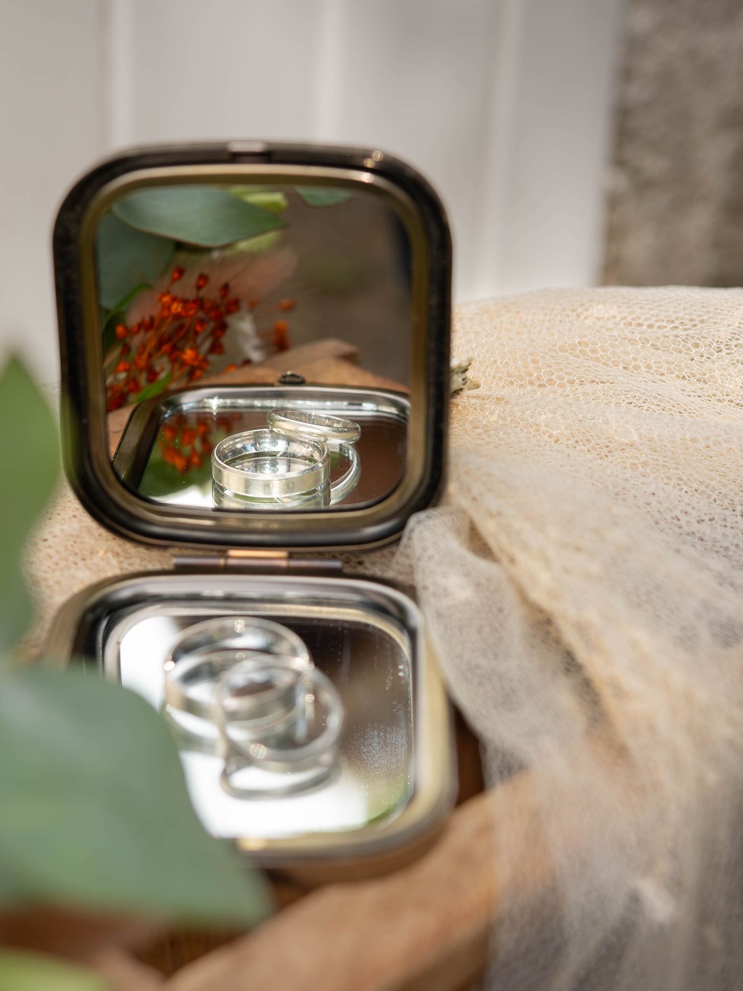 Wedding ring reflected in small vintage compact mirror with lace and floral details.