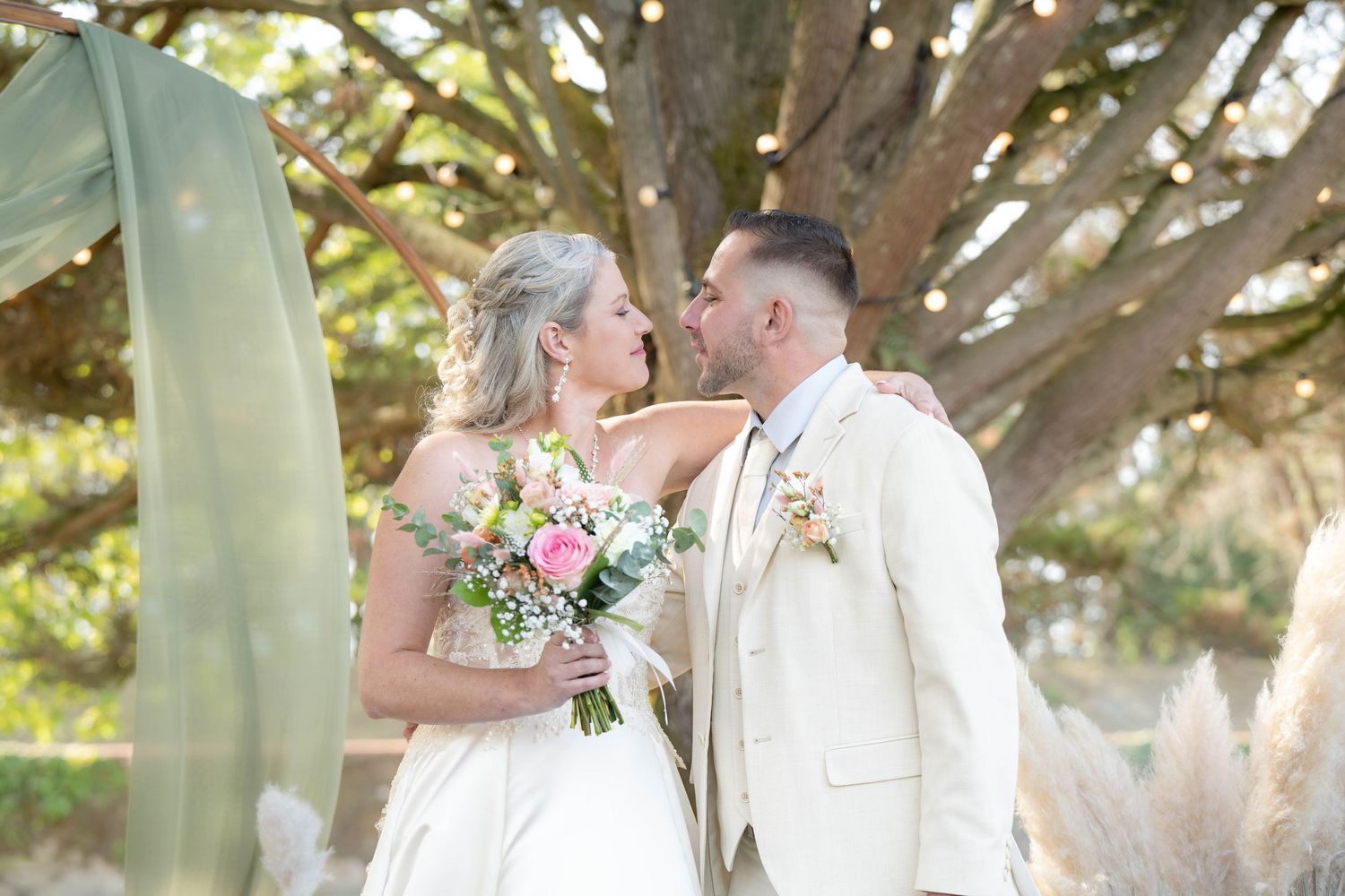 Wedding couple sharing intimate moments under tree branches in natural lighting.