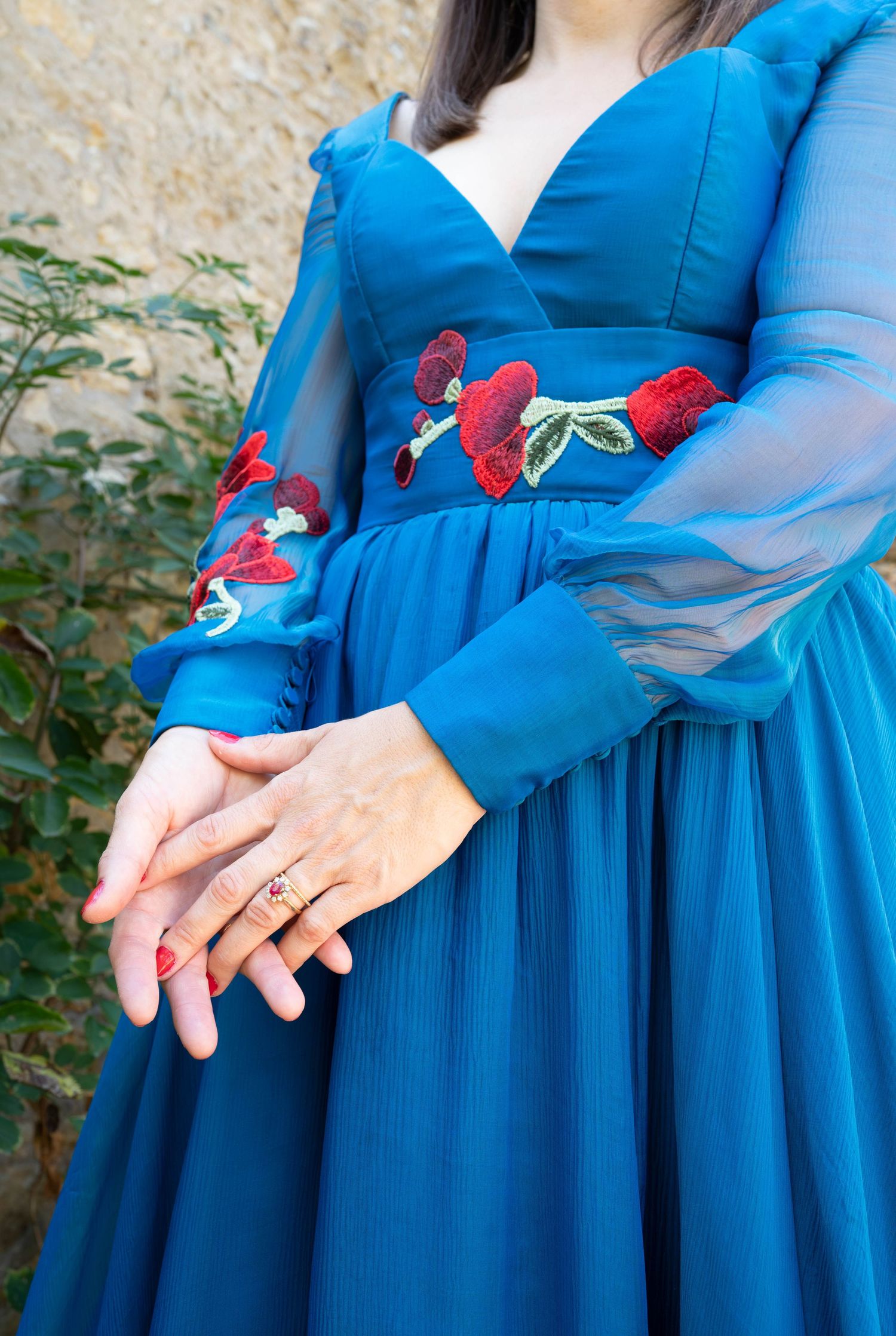 Details of royal blue dress with sheer sleeves and floral embellishments.