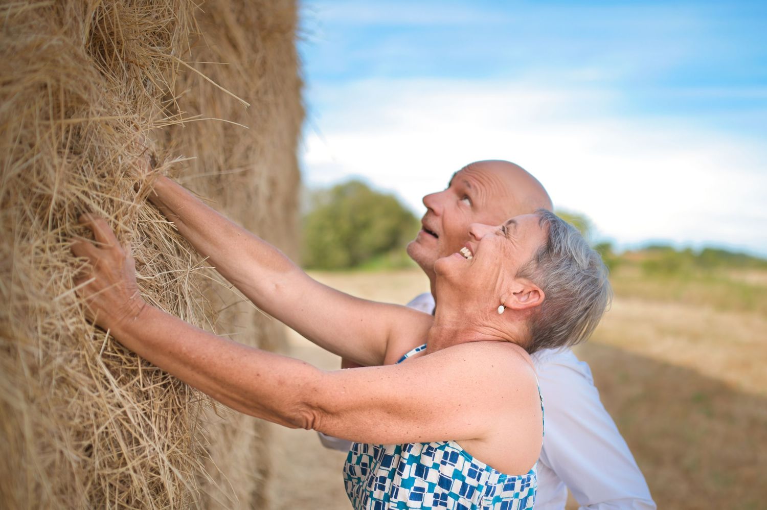 Happy couple enjoying a playful moment together against hay bales in summer field.