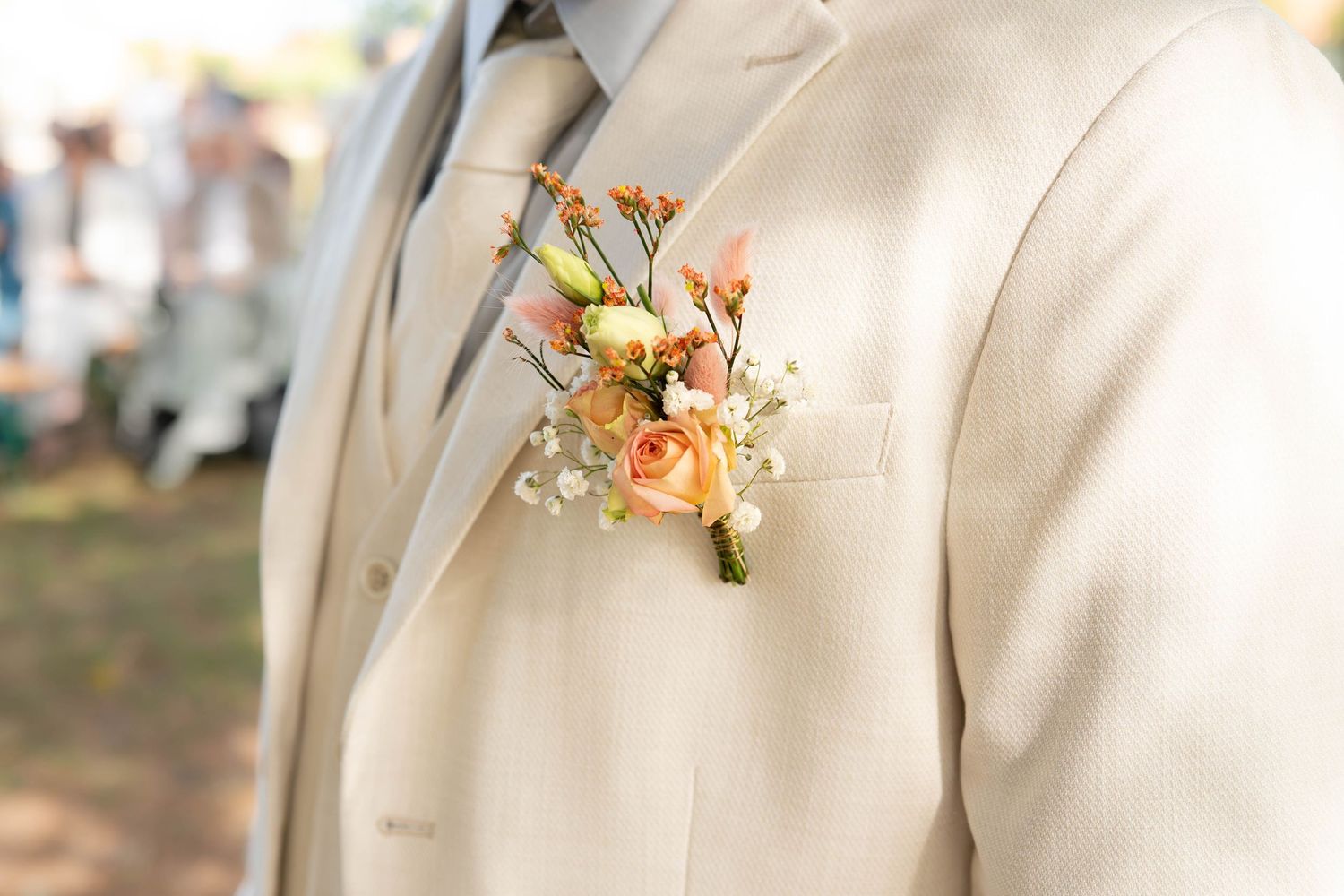 A delicate peach and orange floral boutonniere pinned to a cream-colored suit jacket lapel.