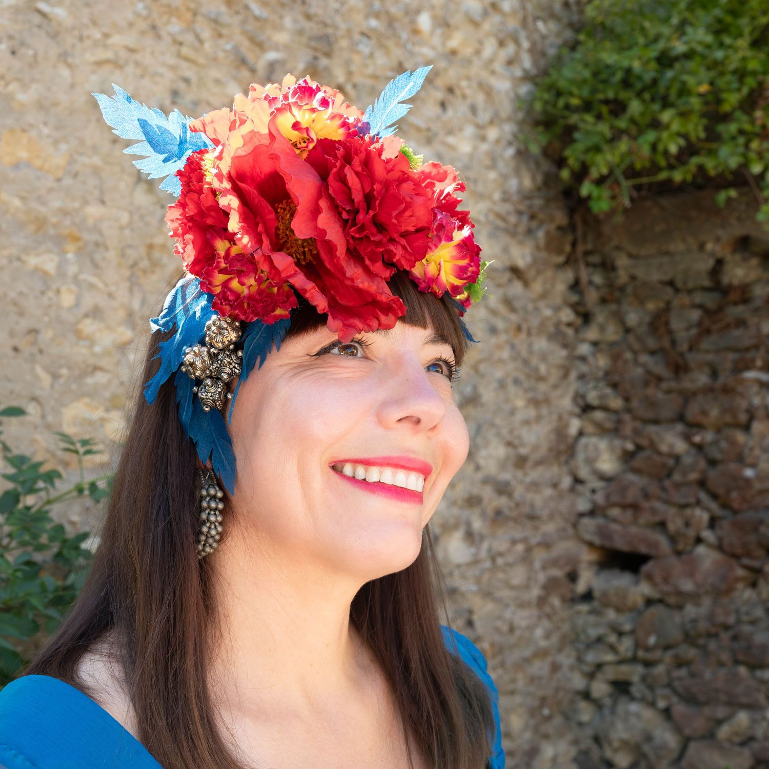 Red floral crown with blue accents captured in outdoor portrait.