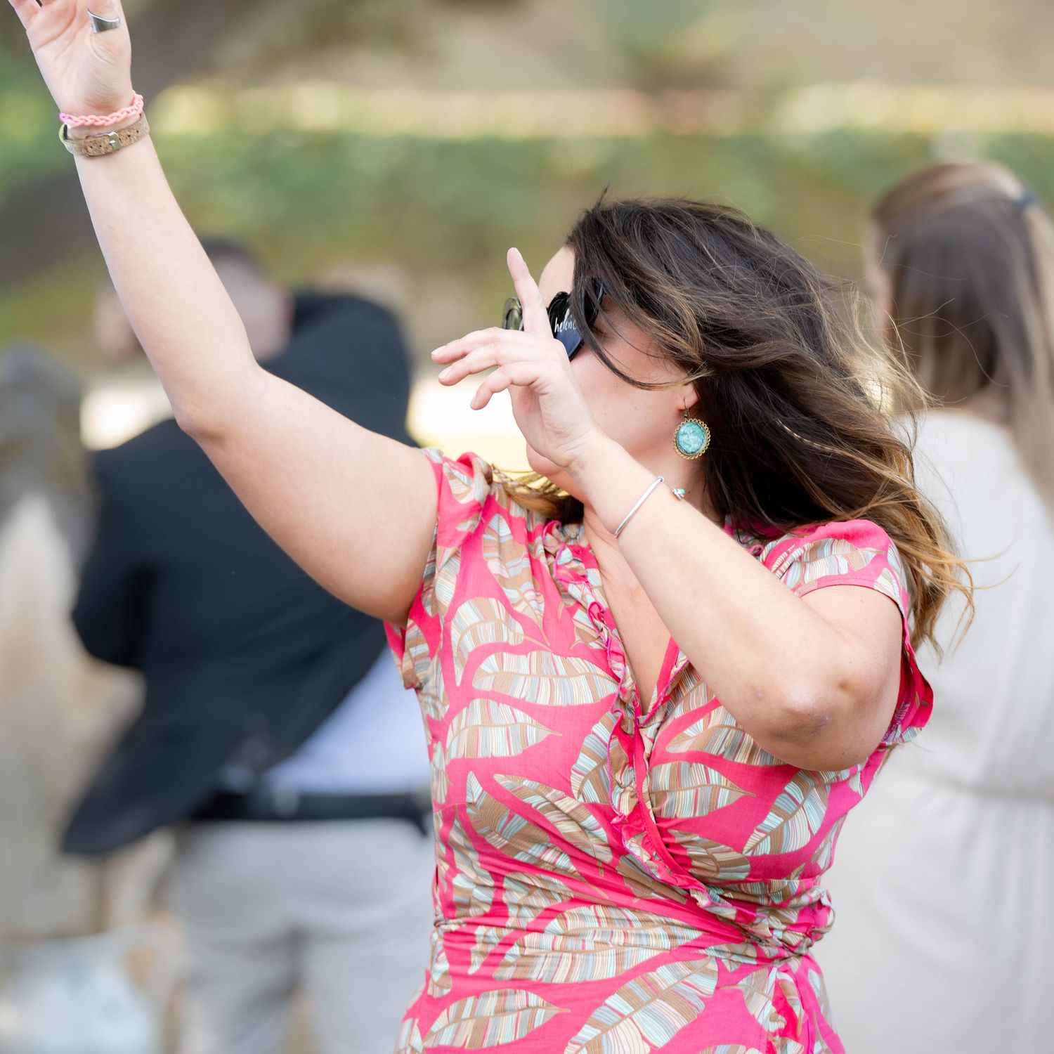 A person in a pink floral dress dances with raised arms in an outdoor setting.