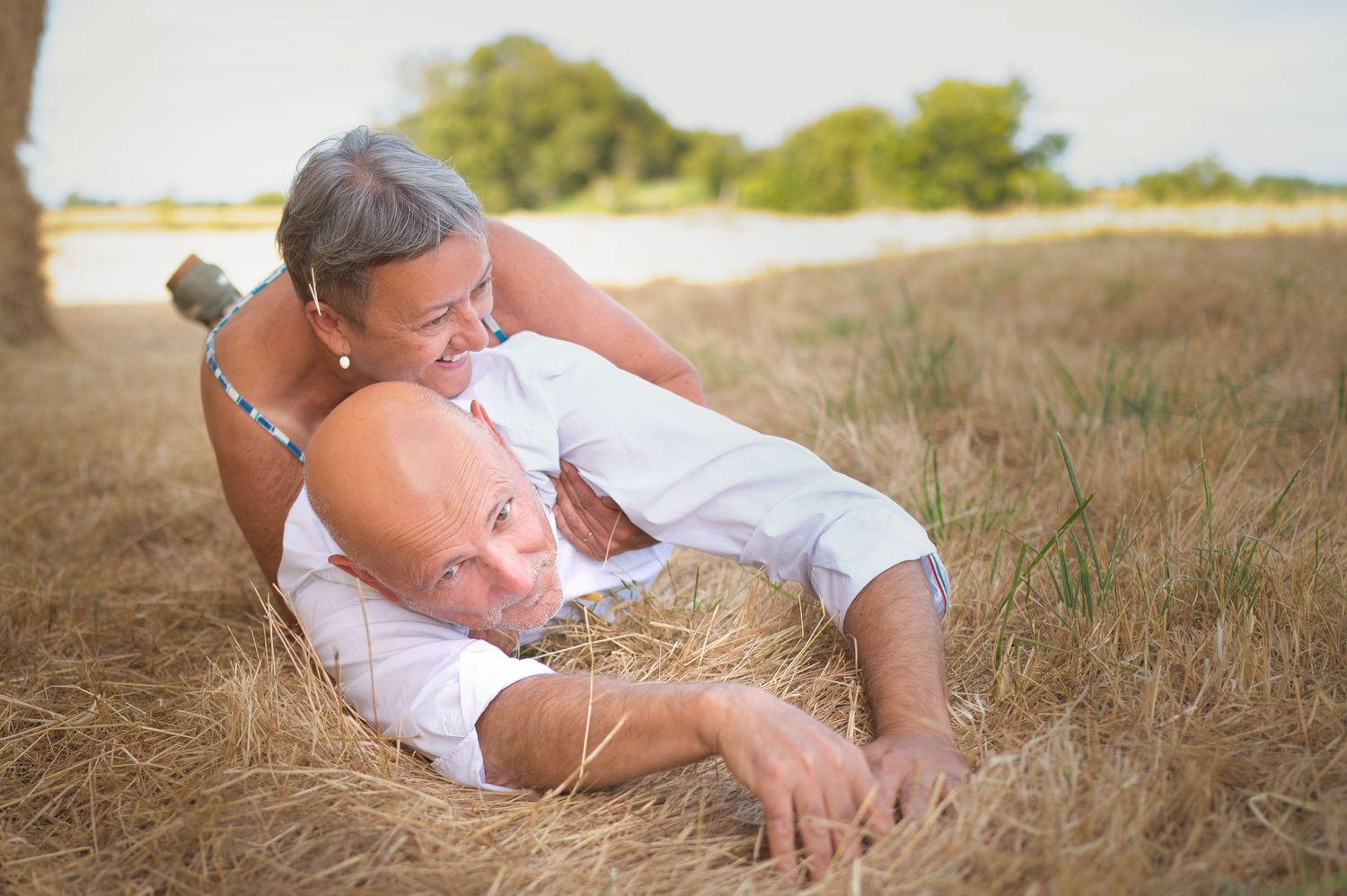 Couple embracing while lying in meadow grass during summer.