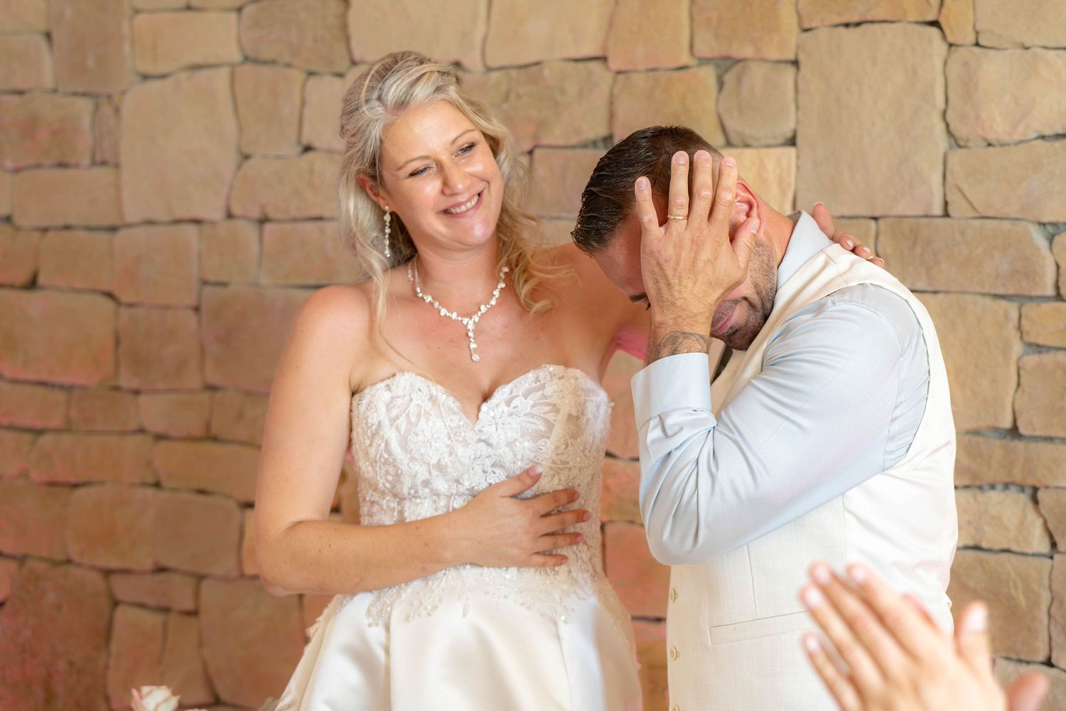 Couple dancing against rustic stone wall backdrop at wedding venue.