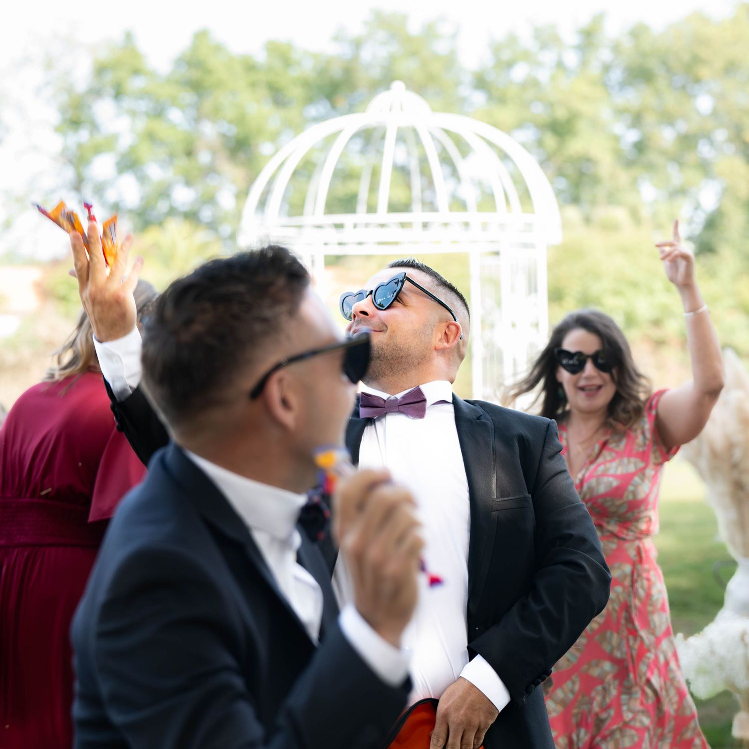 Wedding guests dance and celebrate together outdoors during a sunny daytime reception.