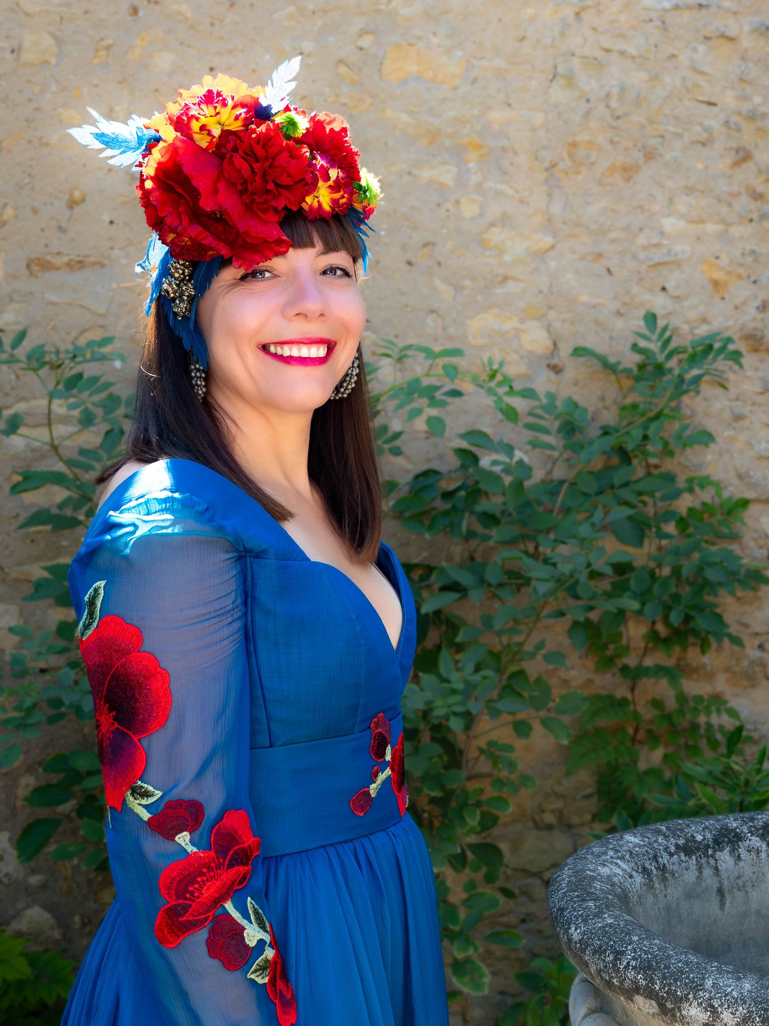 Vibrant blue dress with red floral accents against textured stone wall.