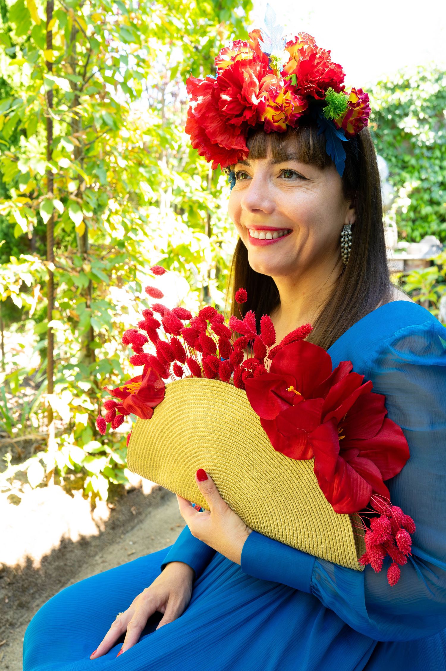 Red floral crown adorns blue dress with yellow fan accessory in garden setting.
