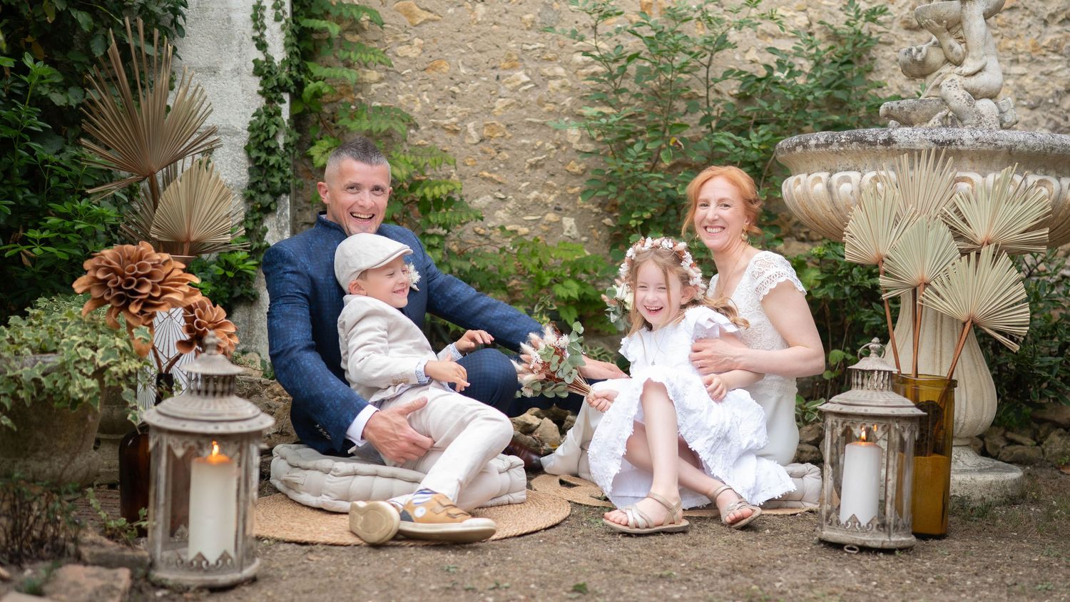 A family sits together outdoors on stone steps with decorative lanterns and a rustic wall backdrop.