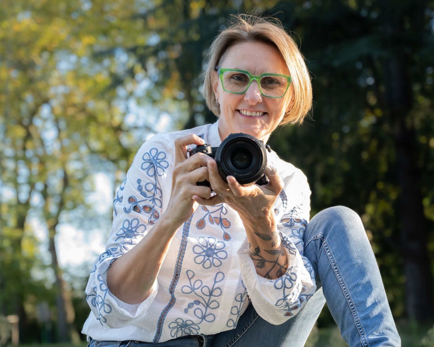 A photographer wearing a blue and white patterned top takes photos outdoors on a sunny day.