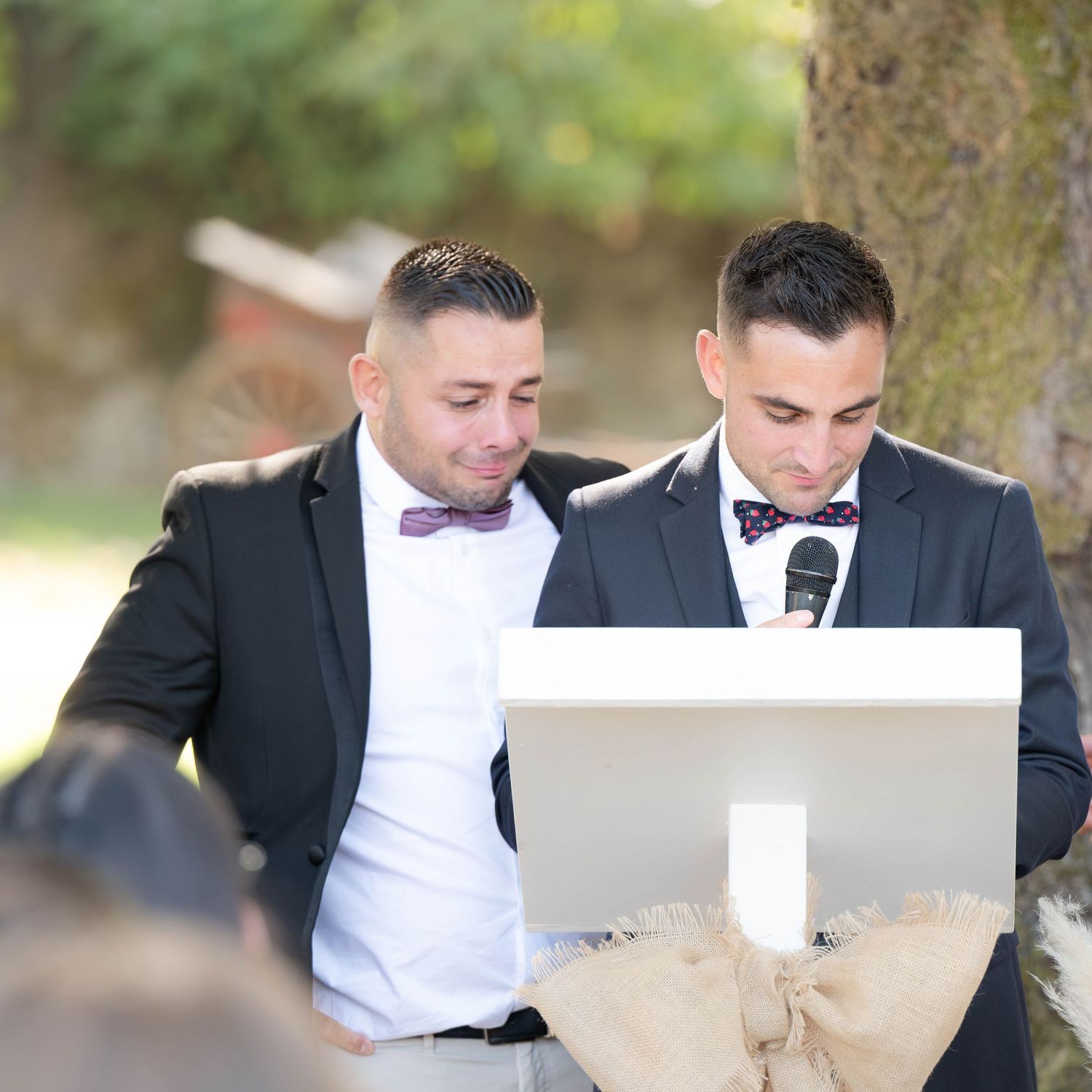 Groomsmen in black suits and bow ties looking at papers while seated outdoors.
