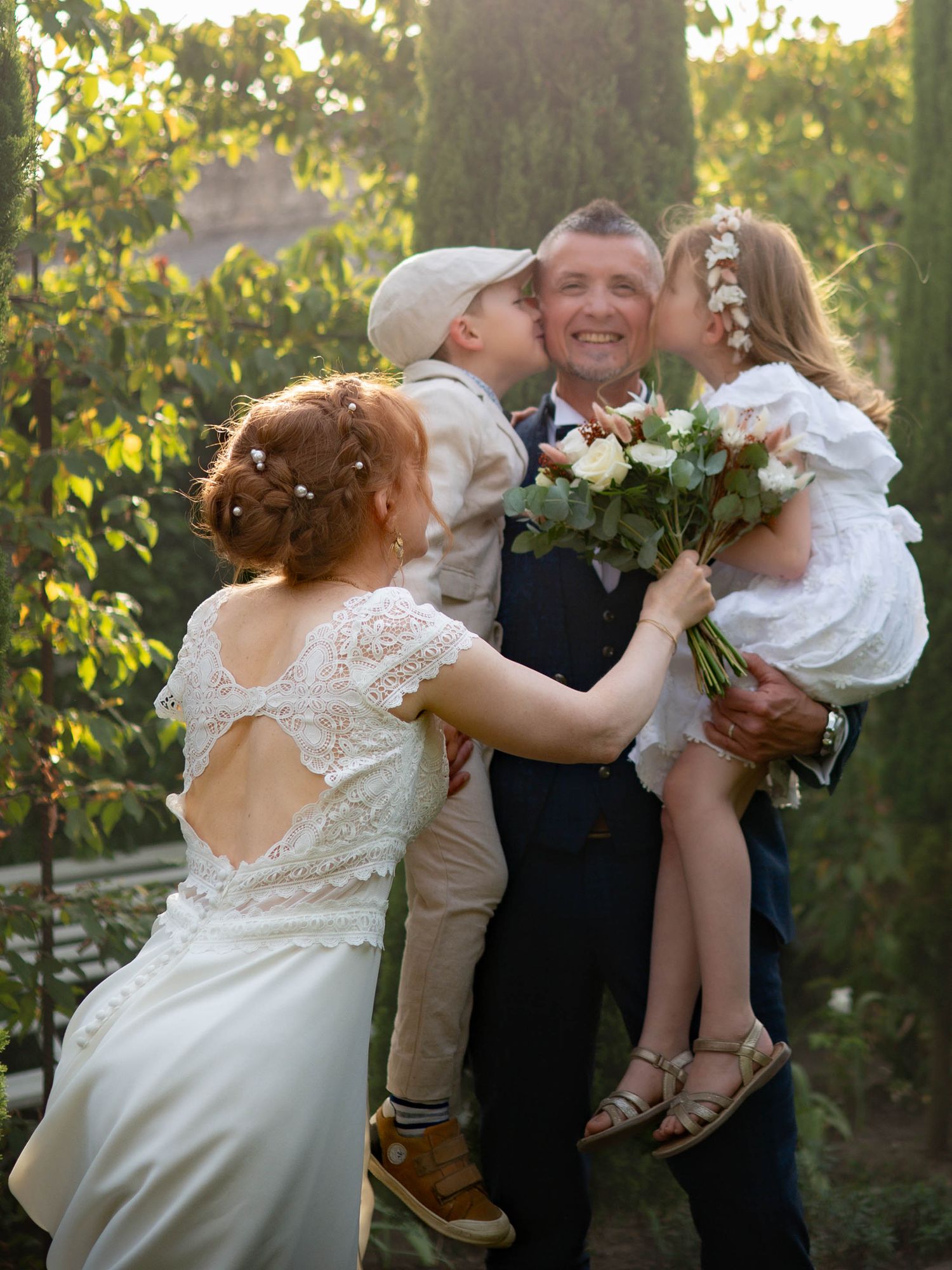 A sweet family moment captured during an outdoor wedding celebration with flowers and golden sunlight in the background.