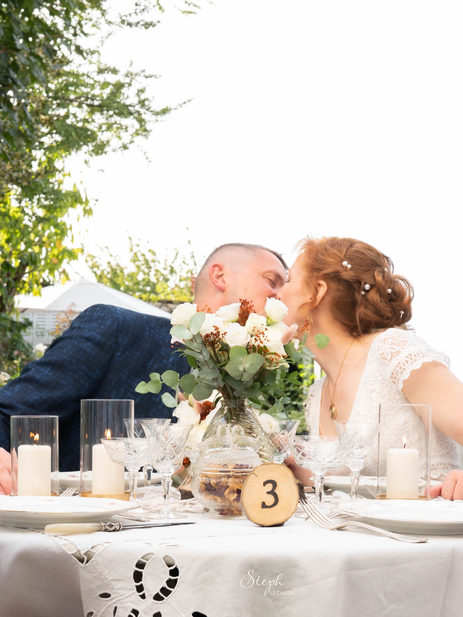 A romantic wedding reception table setting with white flowers, candles and table numbers in an elegant outdoor venue.