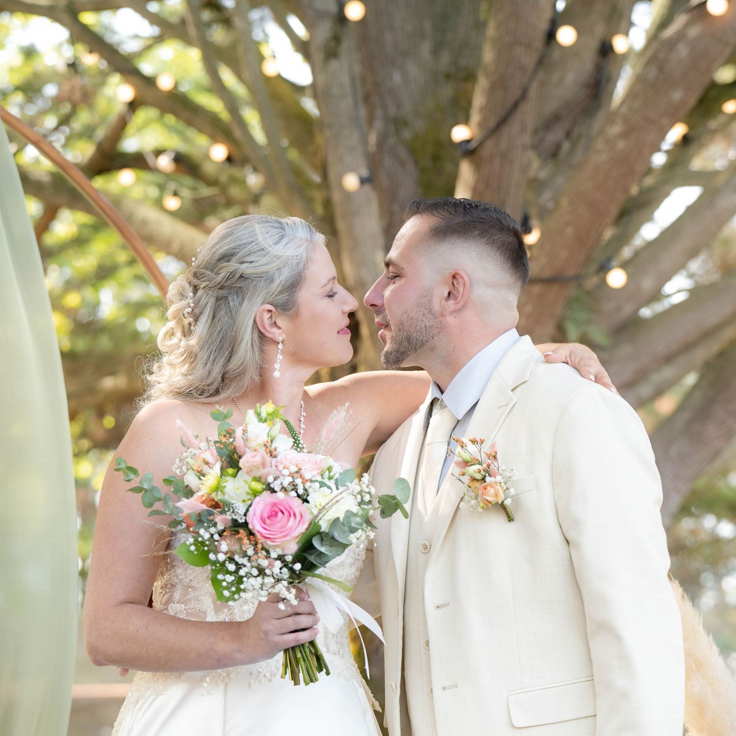 A romantic wedding couple shares tender kisses in a sun-dappled garden setting with soft bokeh lighting effects.