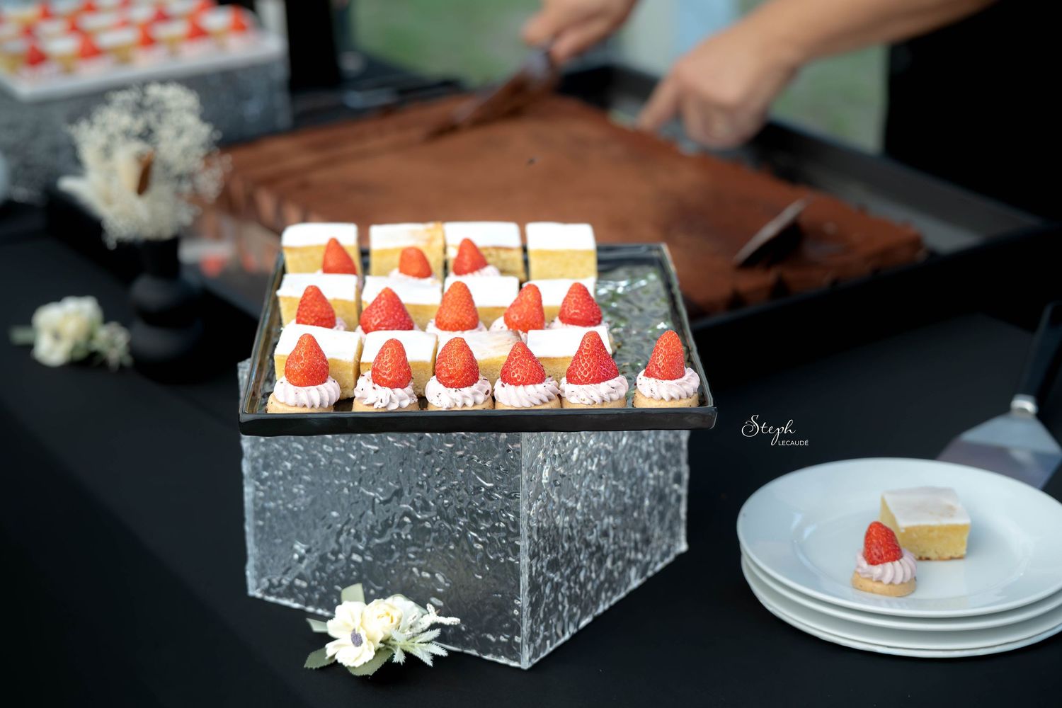 Decorative strawberry and cream dessert bites arranged in rows on a dark serving platter.