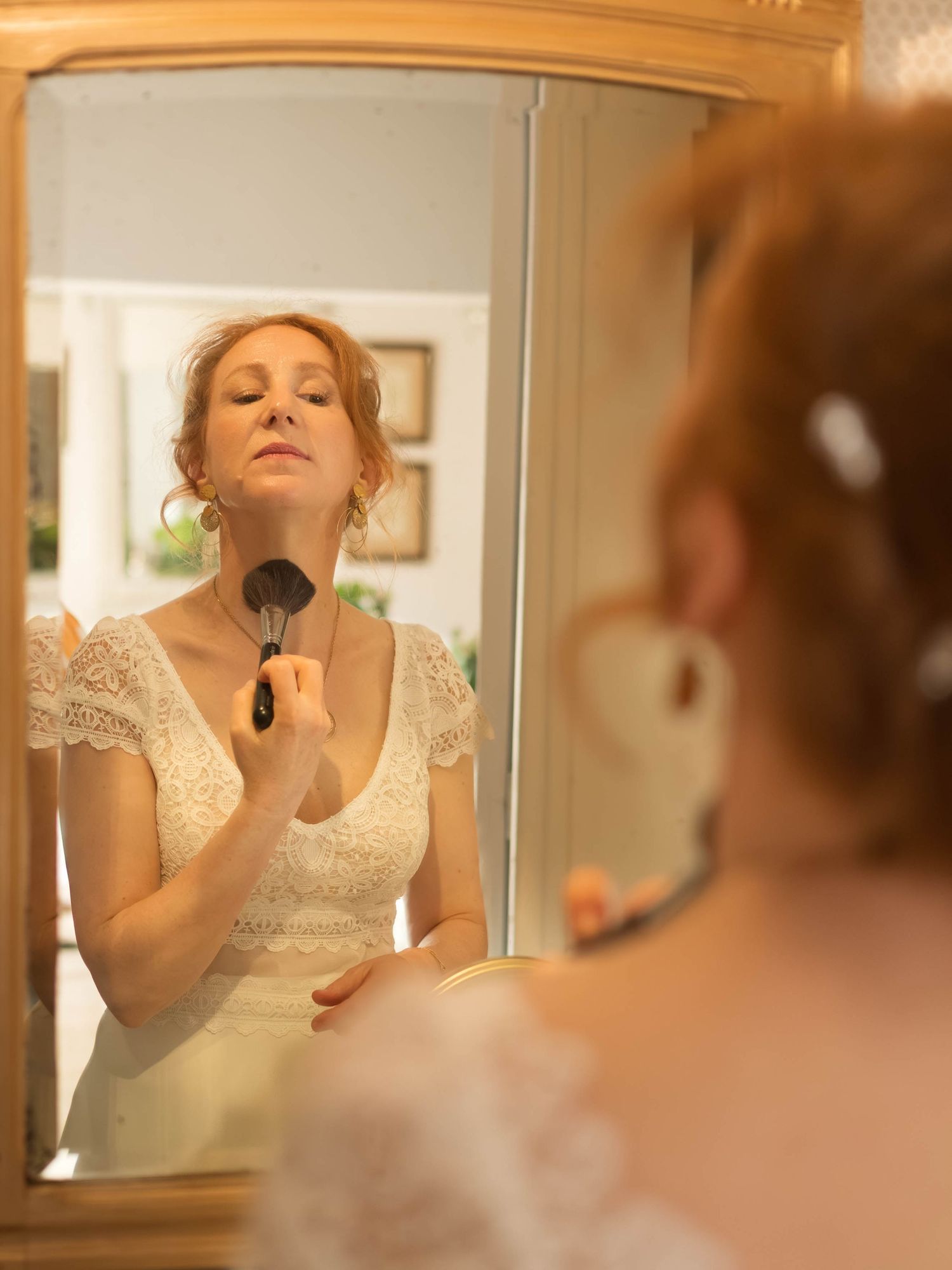 Reflection in vintage mirror shows application of makeup with powder brush.