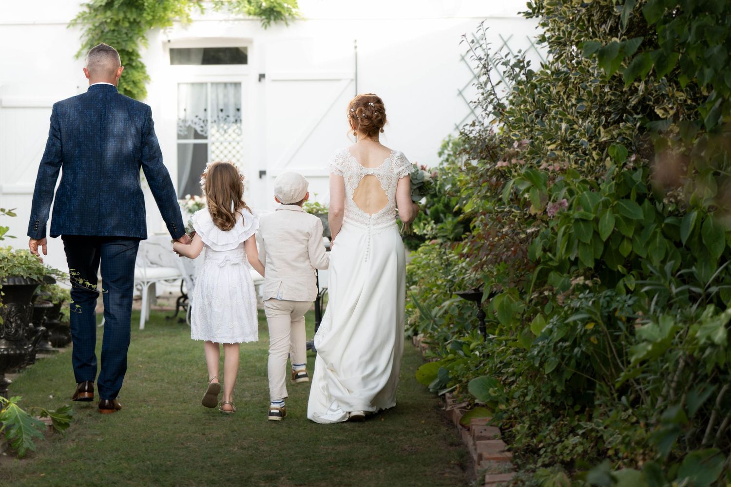 Wedding party walks through a lush garden path during an outdoor ceremony celebration.