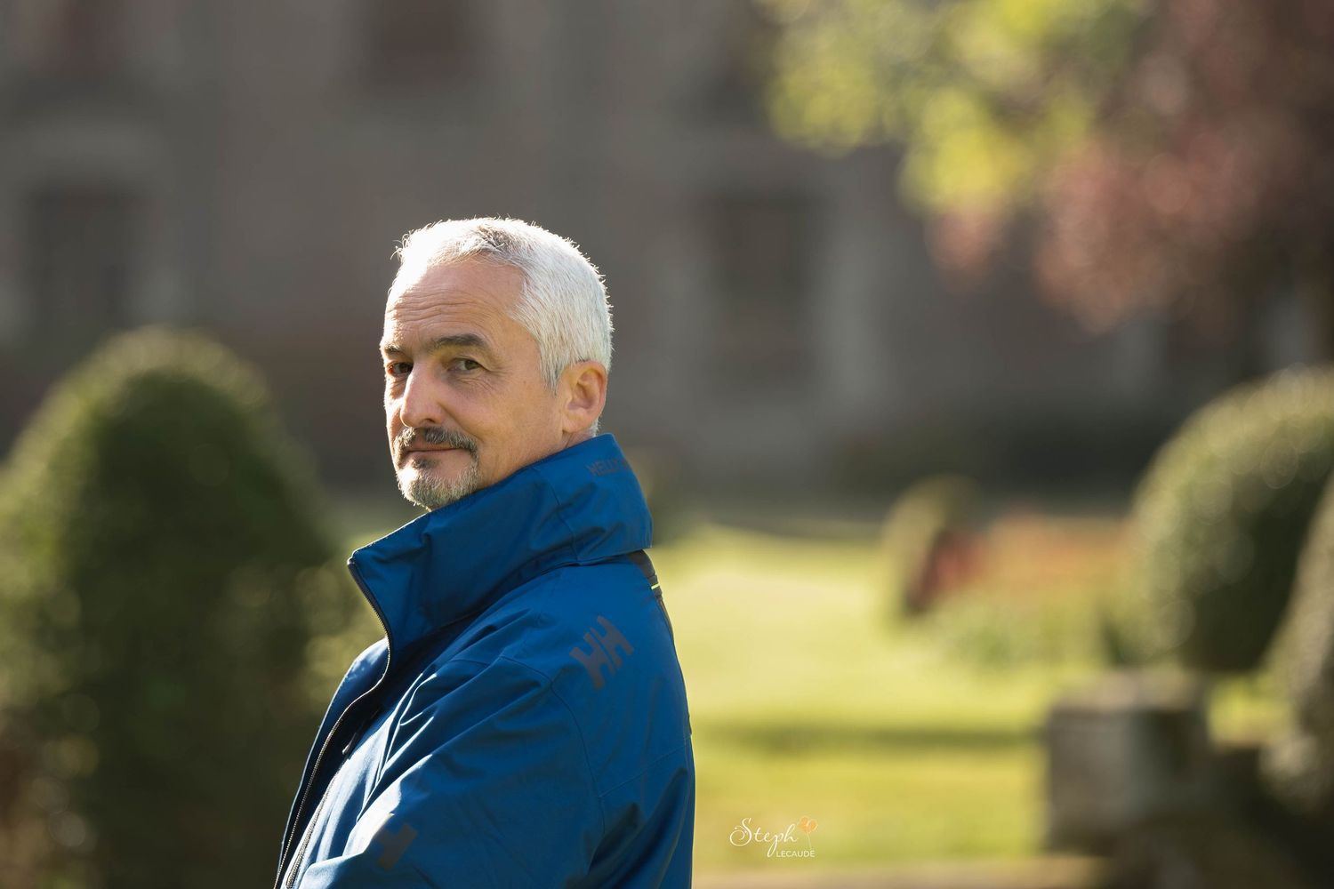 A person in a bright blue jacket looks to the side while standing outdoors on a sunny day.