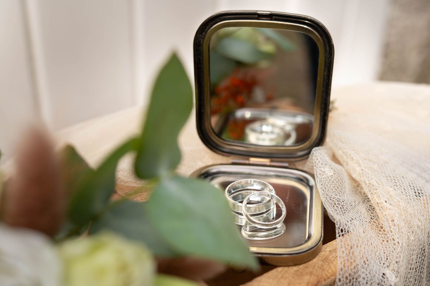 Two gold wedding rings rest on a delicate white lace fabric with soft green foliage in the background.