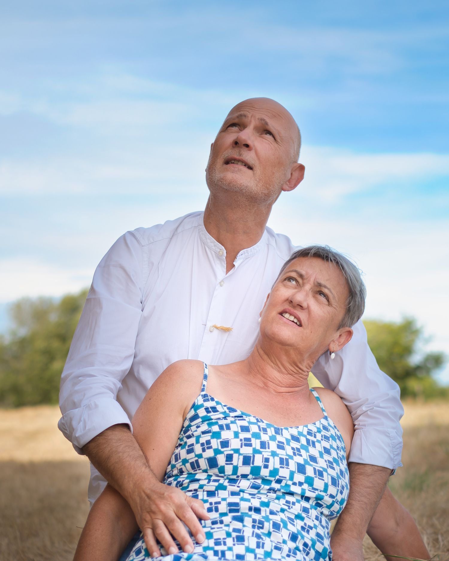 Romantic outdoor photoshoot of a couple in blue and white attire on a grassy hillside.