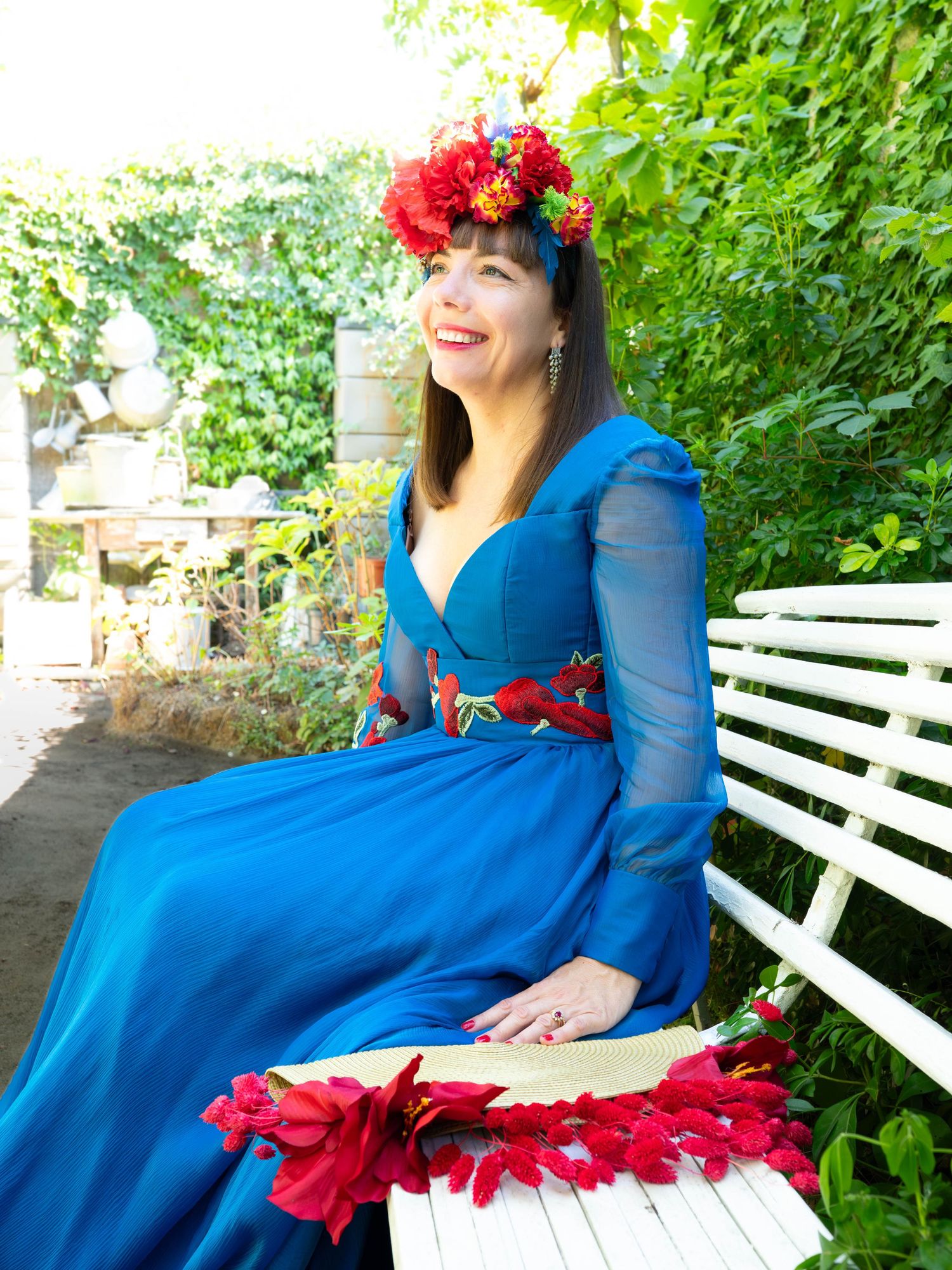 Elegant royal blue dress with red floral crown in a garden setting.