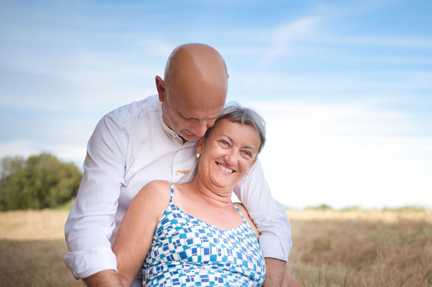 Tender moment between couple lying in golden field with blue sky backdrop.