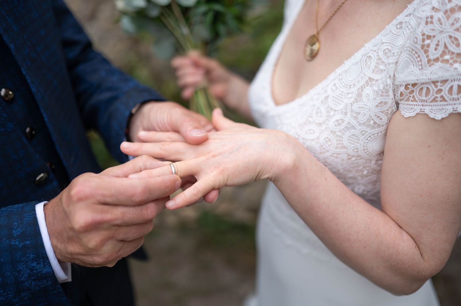 Close-up of hands exchanging wedding rings during ceremony with lace dress detail.
