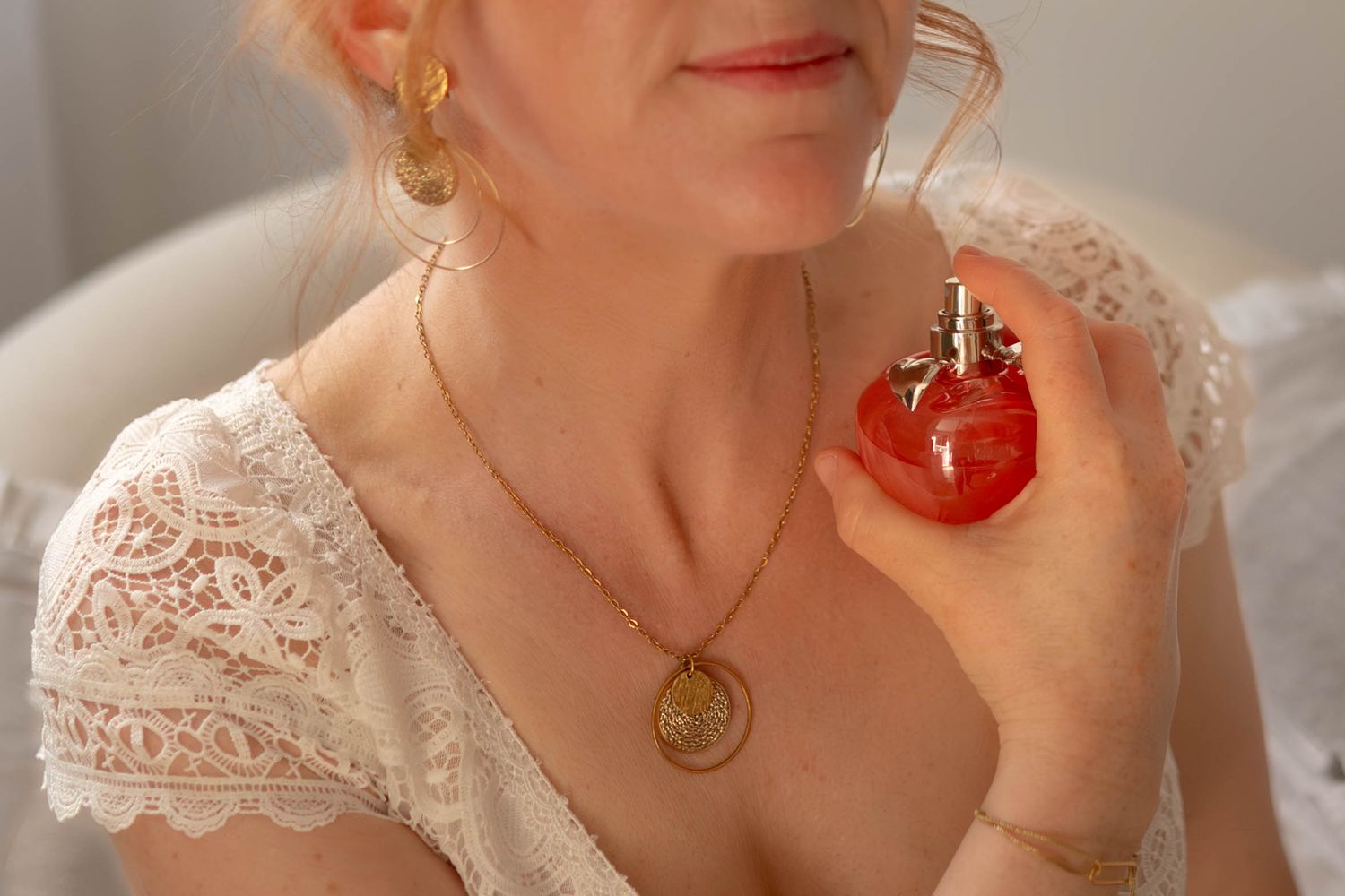 Close-up of lace dress detail with gold pendant necklace and perfume bottle.