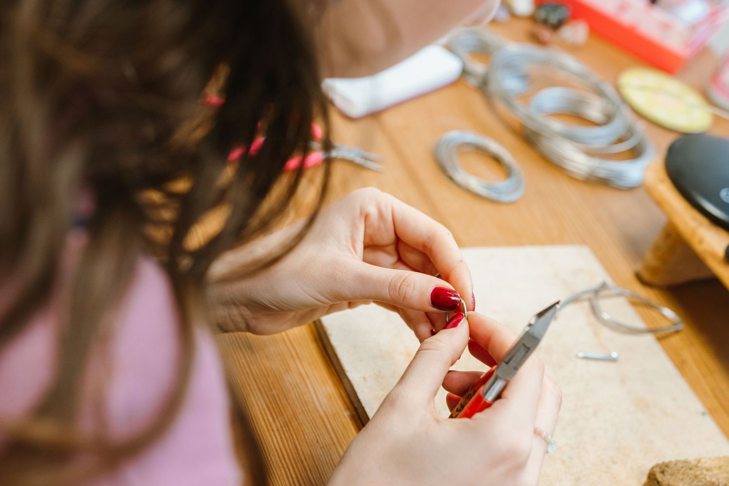 Close-up of hands working on handmade jewelry pieces at a wooden table.