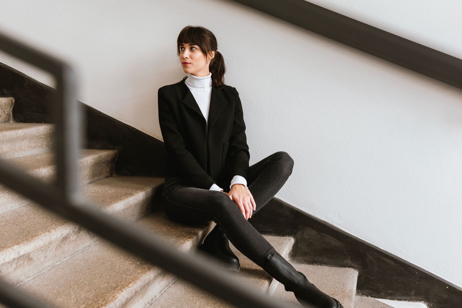 Person sitting in black outfit against architectural backdrop in contemporary setting.