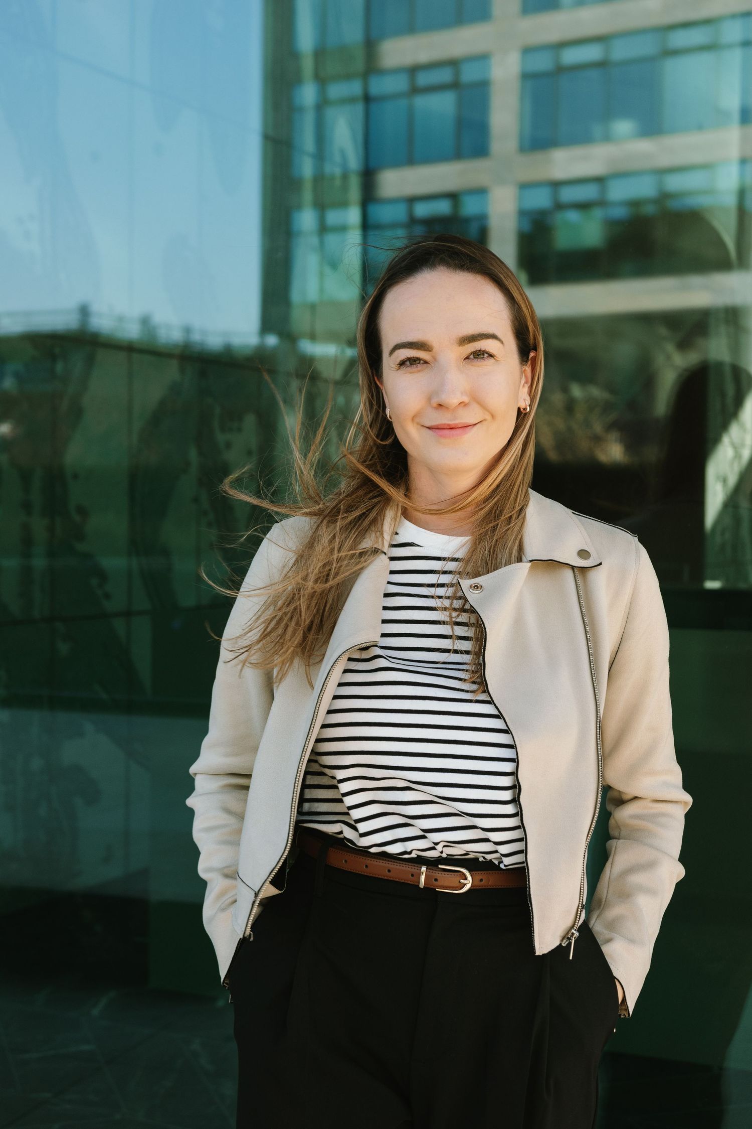 Portrait of person in striped top and beige jacket against modern building.