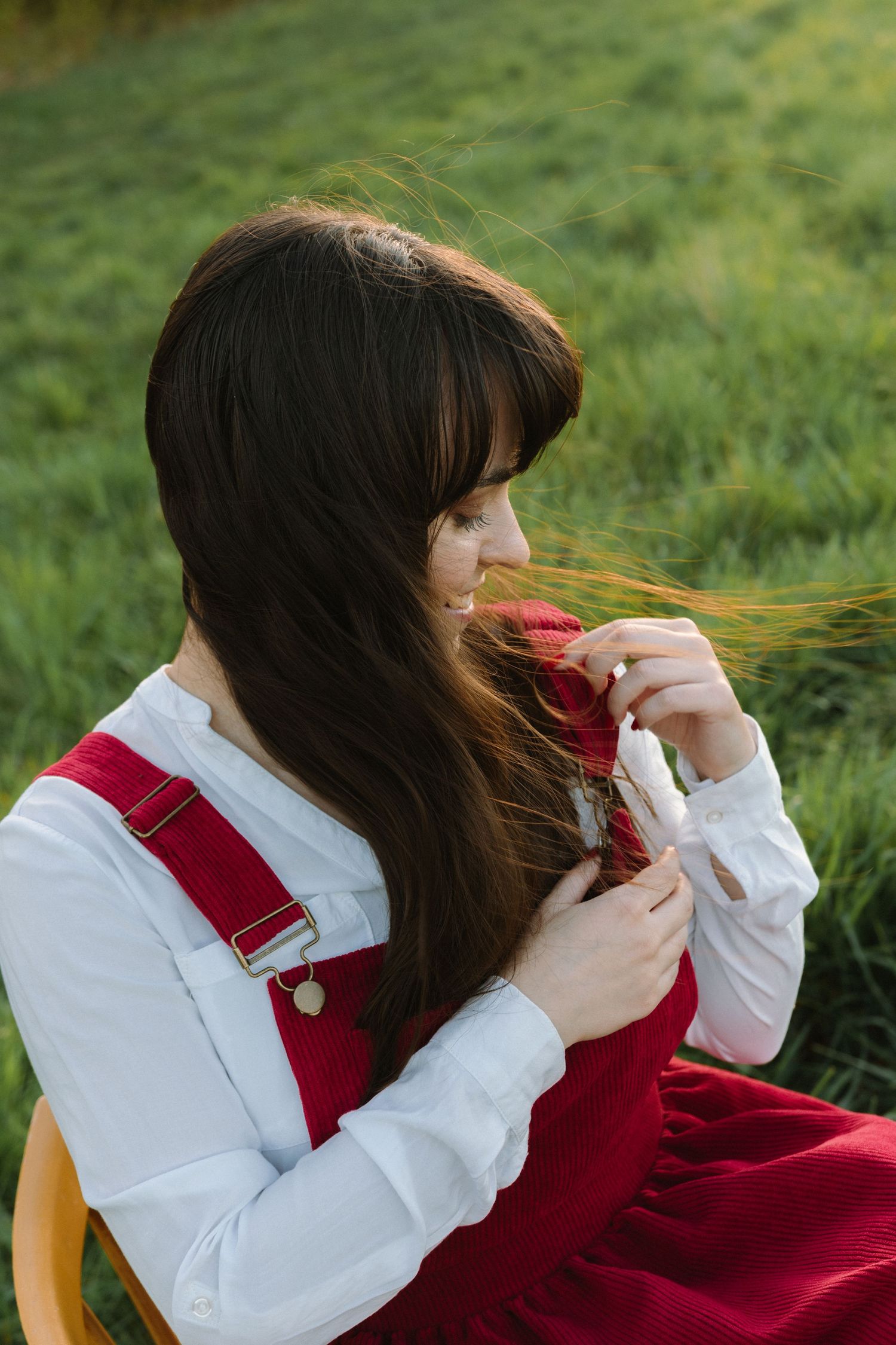 A person in a red dress and white top sits on a chair outdoors playing with their long dark hair.