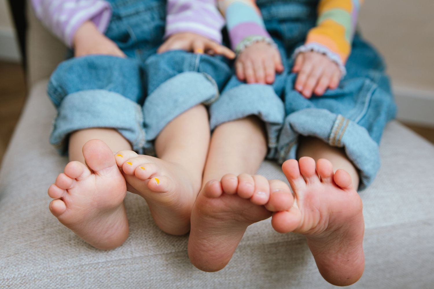 Close-up view of bare feet lined up in a row, showing toes and rolled-up jeans on a couch.