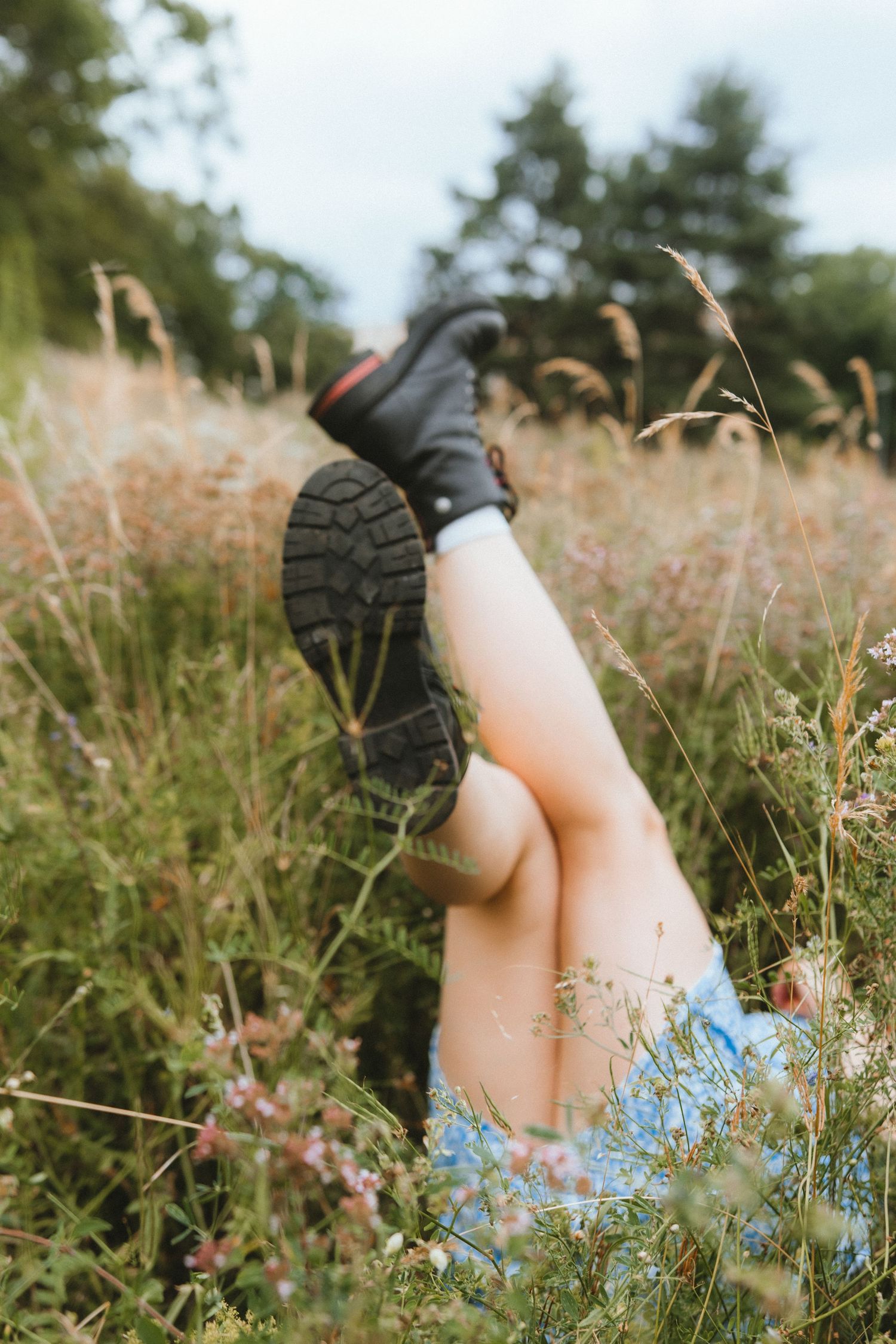 A pair of black boots and legs visible among tall grass and wildflowers in a whimsical outdoor setting.