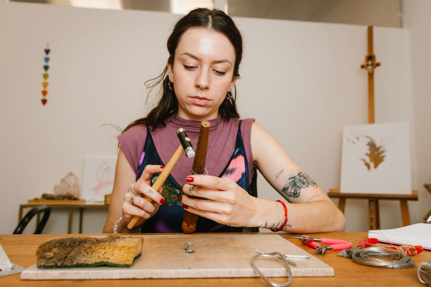 Someone wearing a purple sleeveless top works on crafting jewelry at a wooden workbench.