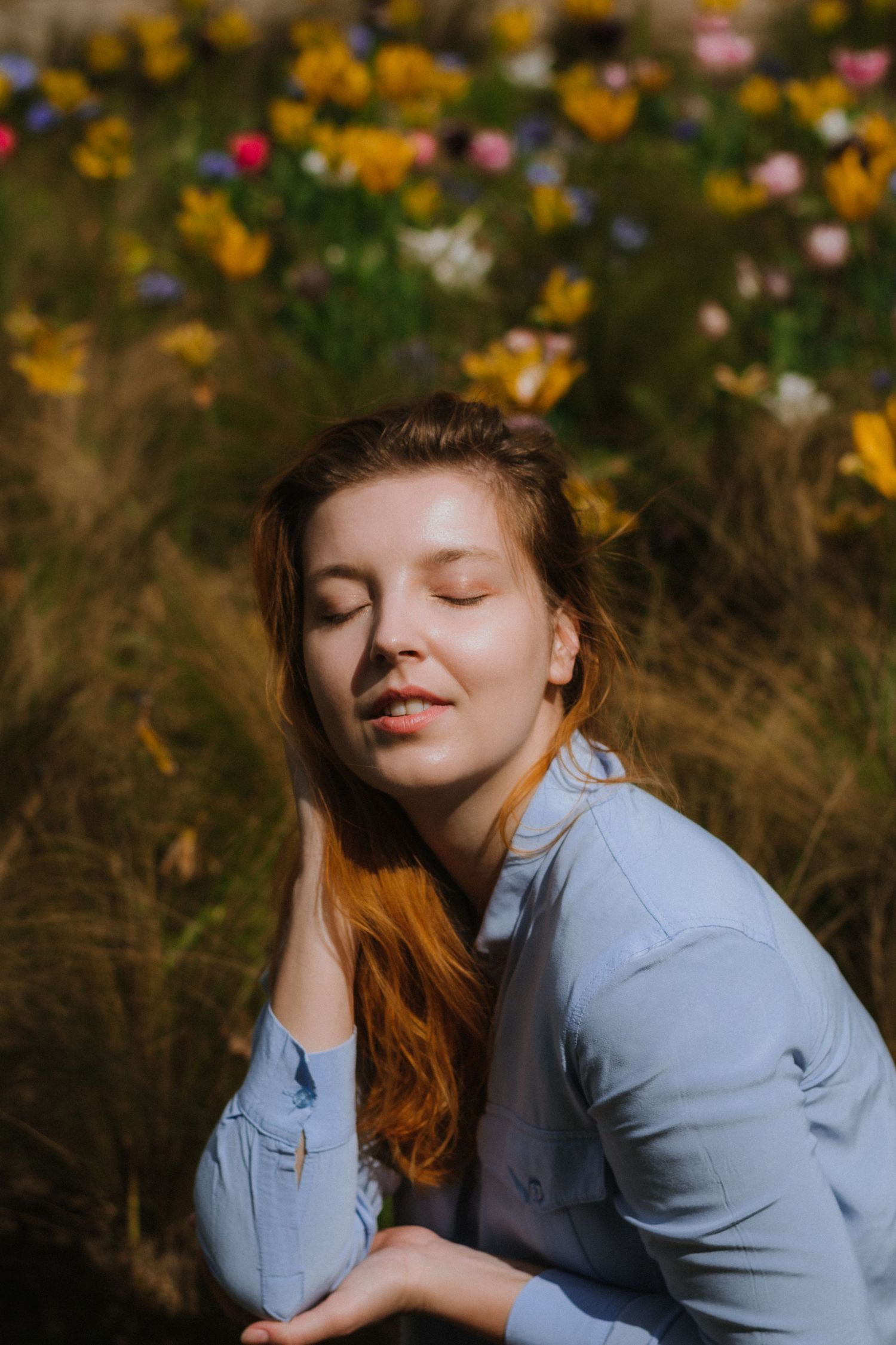 Person in light blue shirt posing in field of yellow wildflowers during sunset.