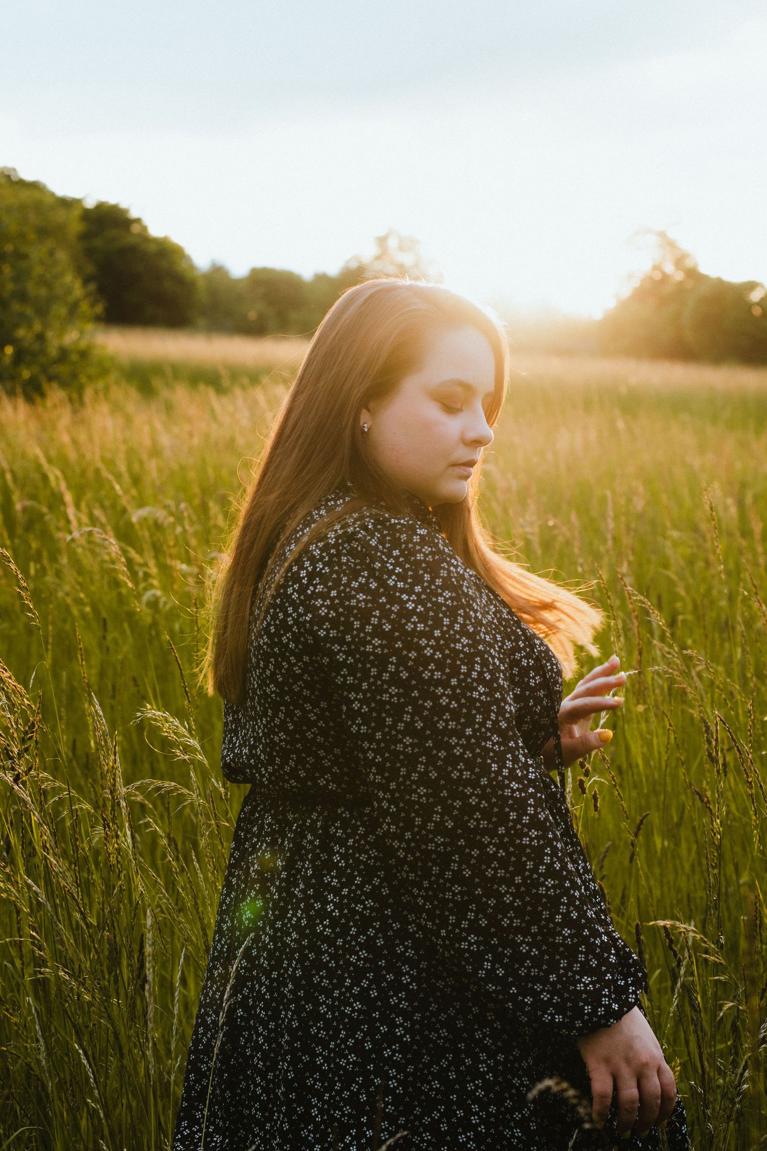 Silhouette of someone in a patterned dress standing in tall grass during golden hour.