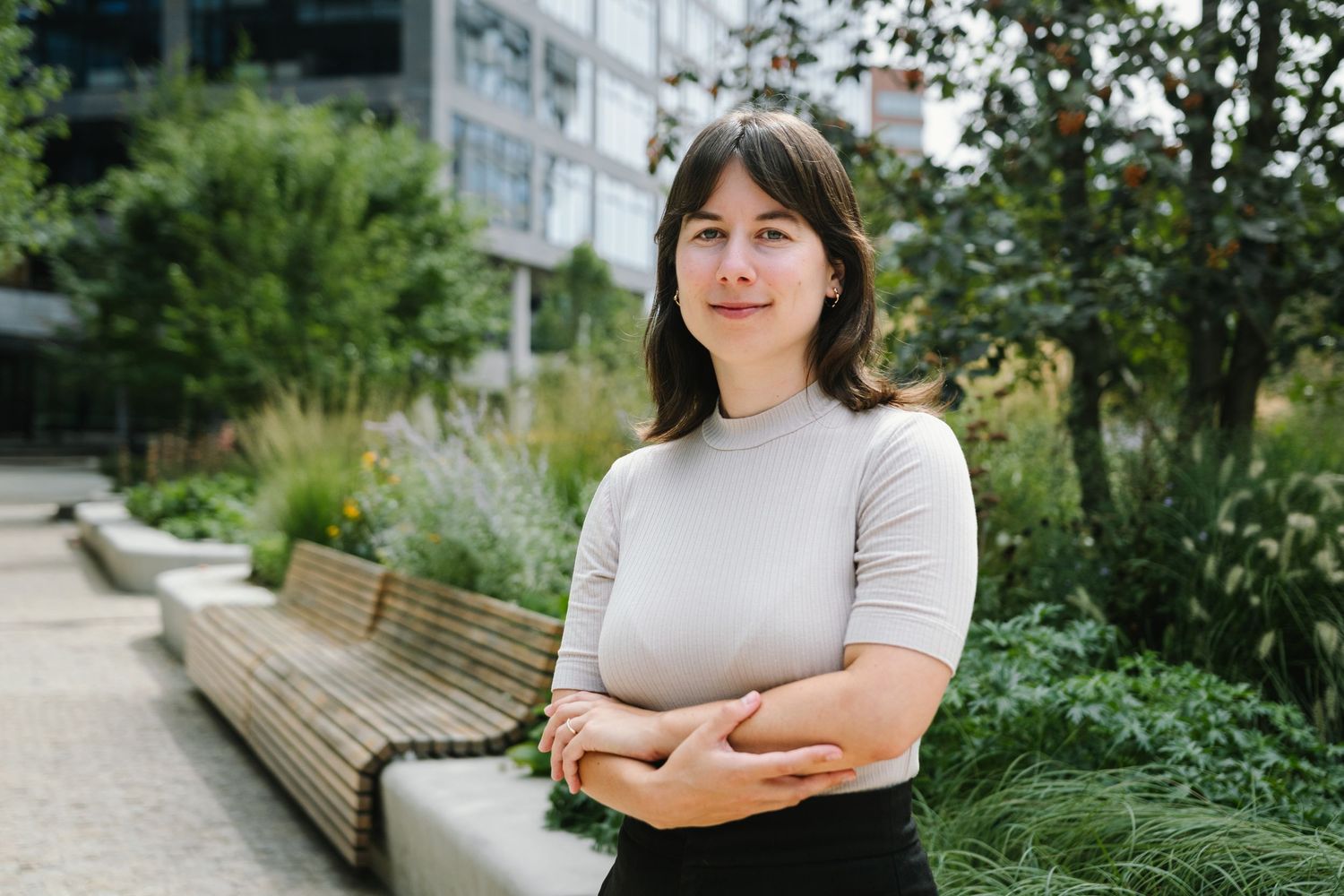 A person in a light colored top sits on an outdoor bench near urban landscaping.