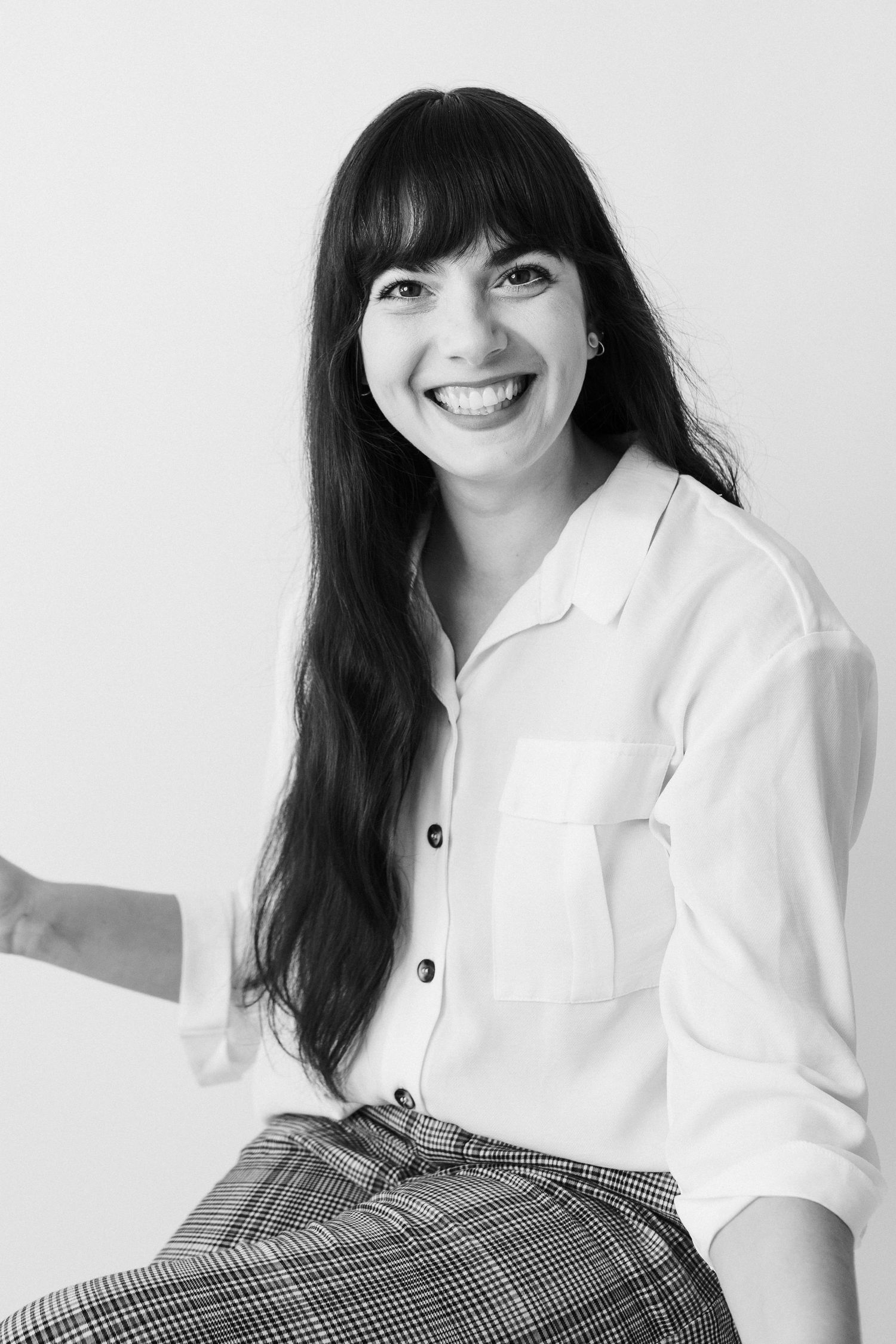Black and white professional headshot featuring a classic white button-up shirt and plaid skirt.