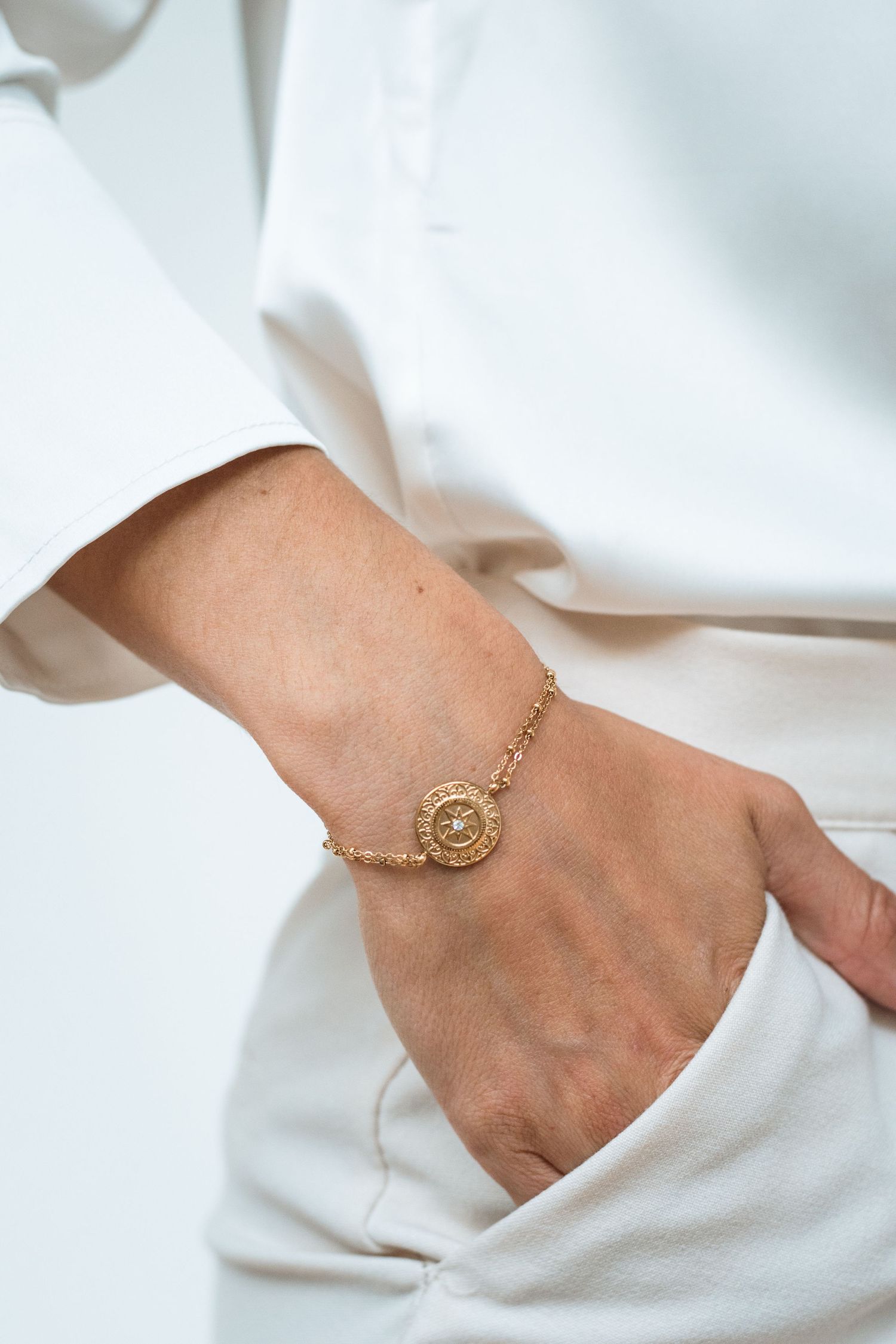 Elegant gold chain bracelet with circular medallion charm displayed on wrist against white fabric.
