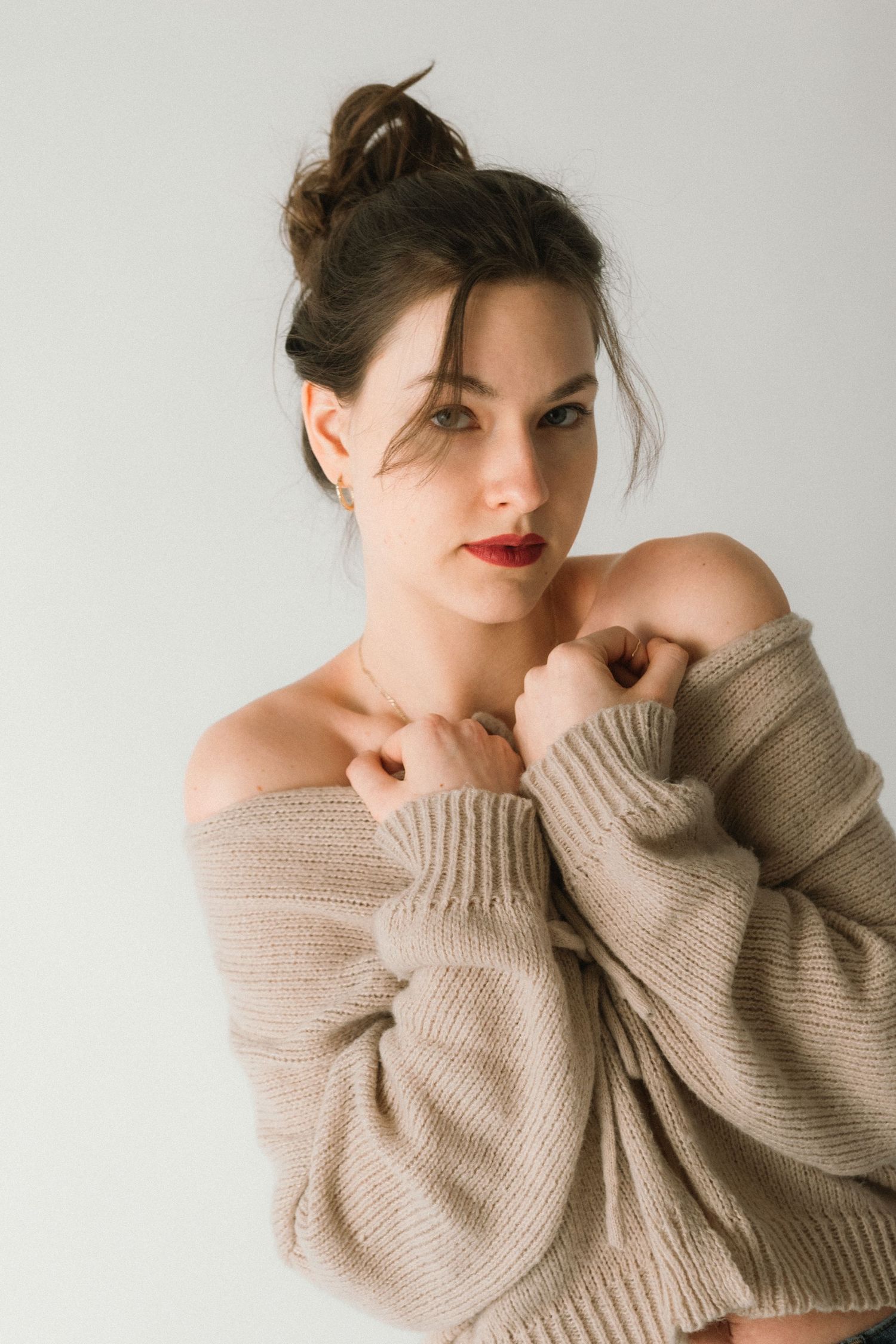 Person in beige sweater posing artistically against white background.
