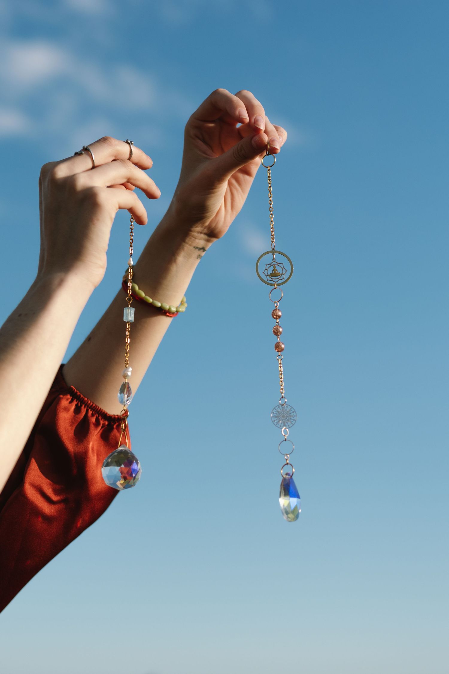 Hands hold up a decorative crystal suncatcher against bright blue sky.