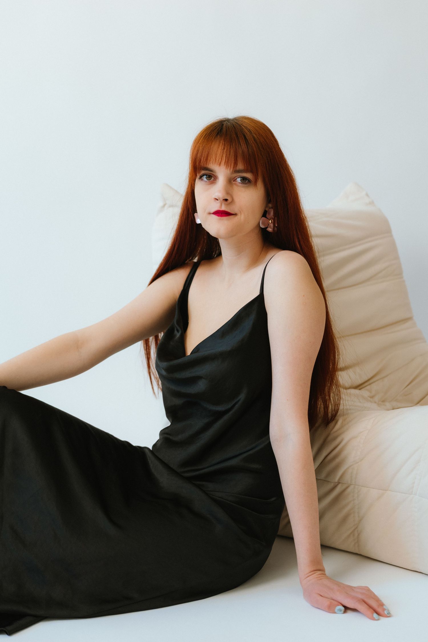 A woman in a black slip dress reclines on white cushions in a minimalist setting.